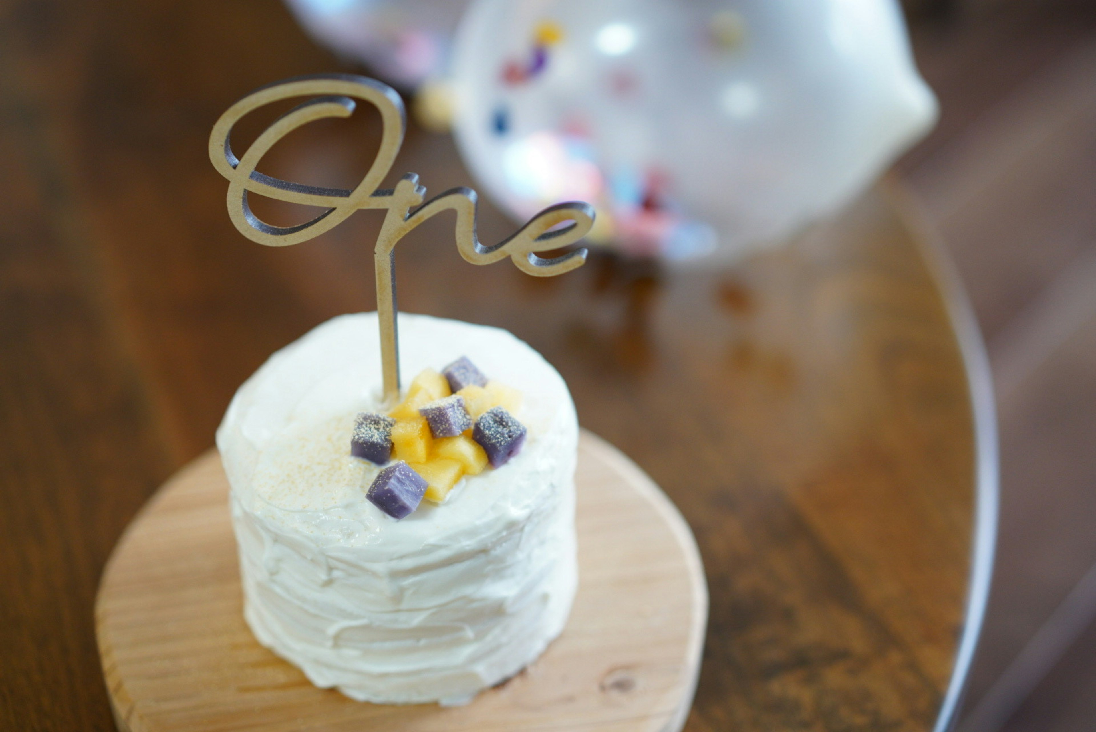 Small white frosted cake with a golden 'One' topper and fruit decorations