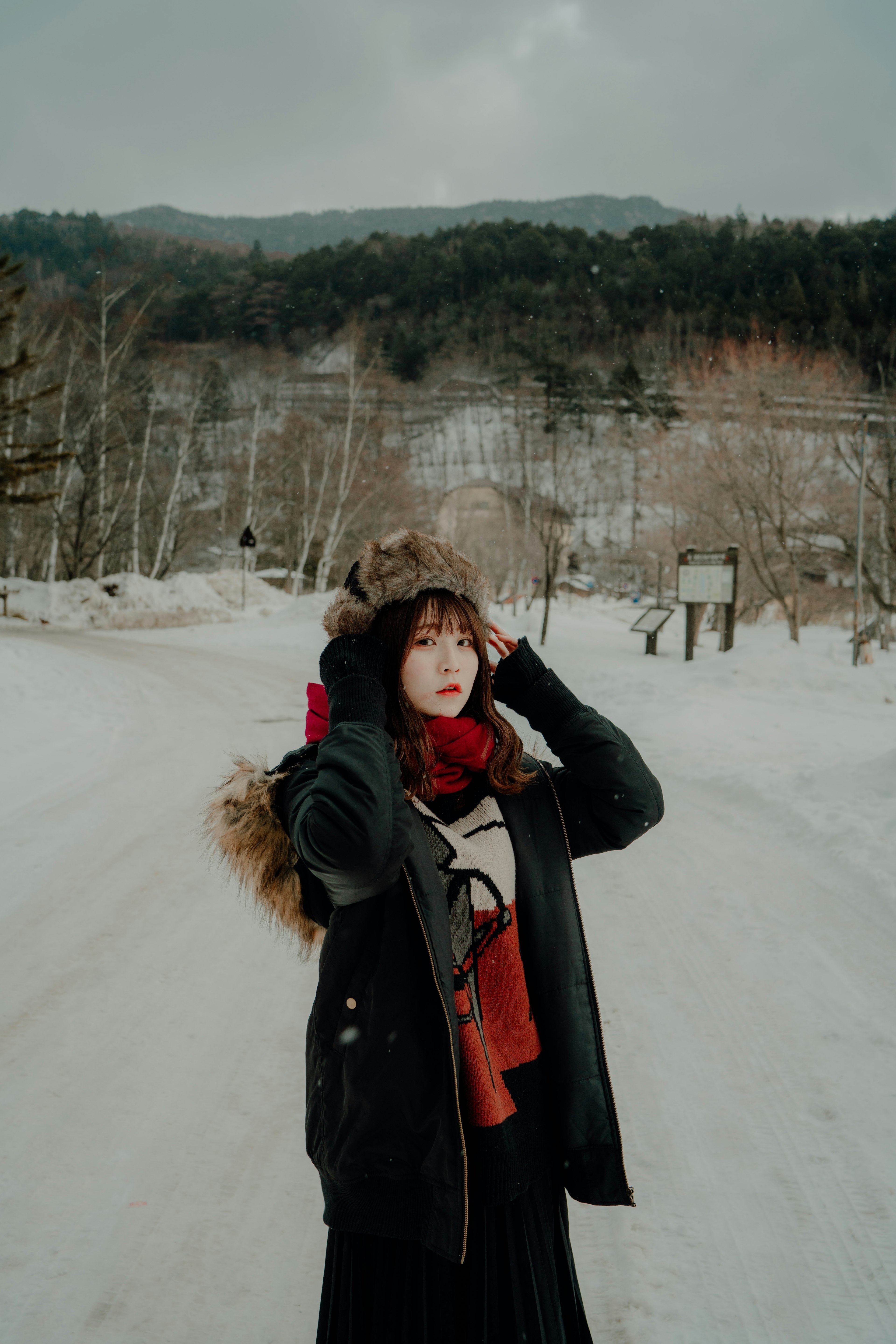 穿着冬装的女性在雪覆盖的风景中捂着头，背景有山和树