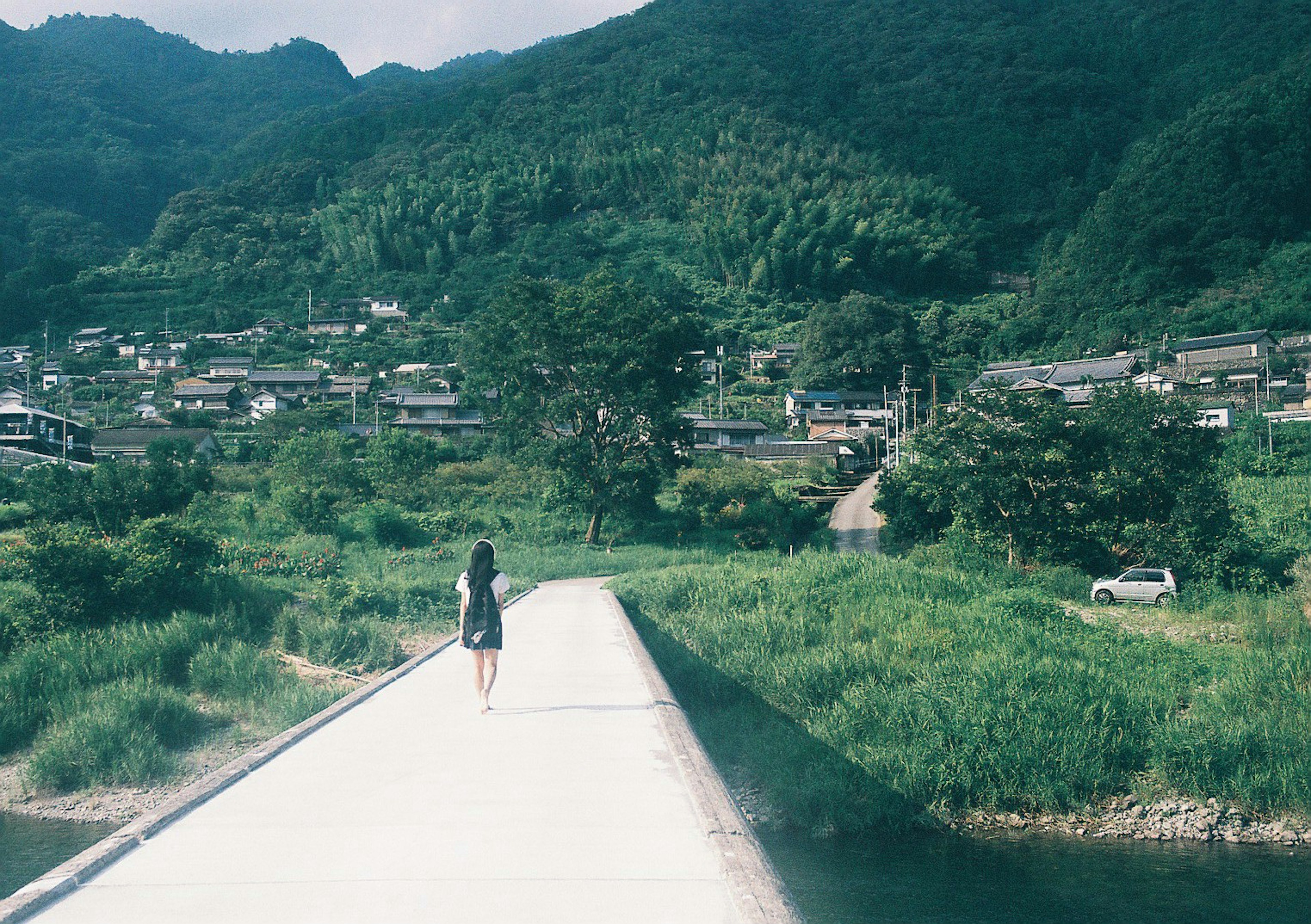 Une femme marchant sur un chemin avec des montagnes verdoyantes et un village serein en arrière-plan