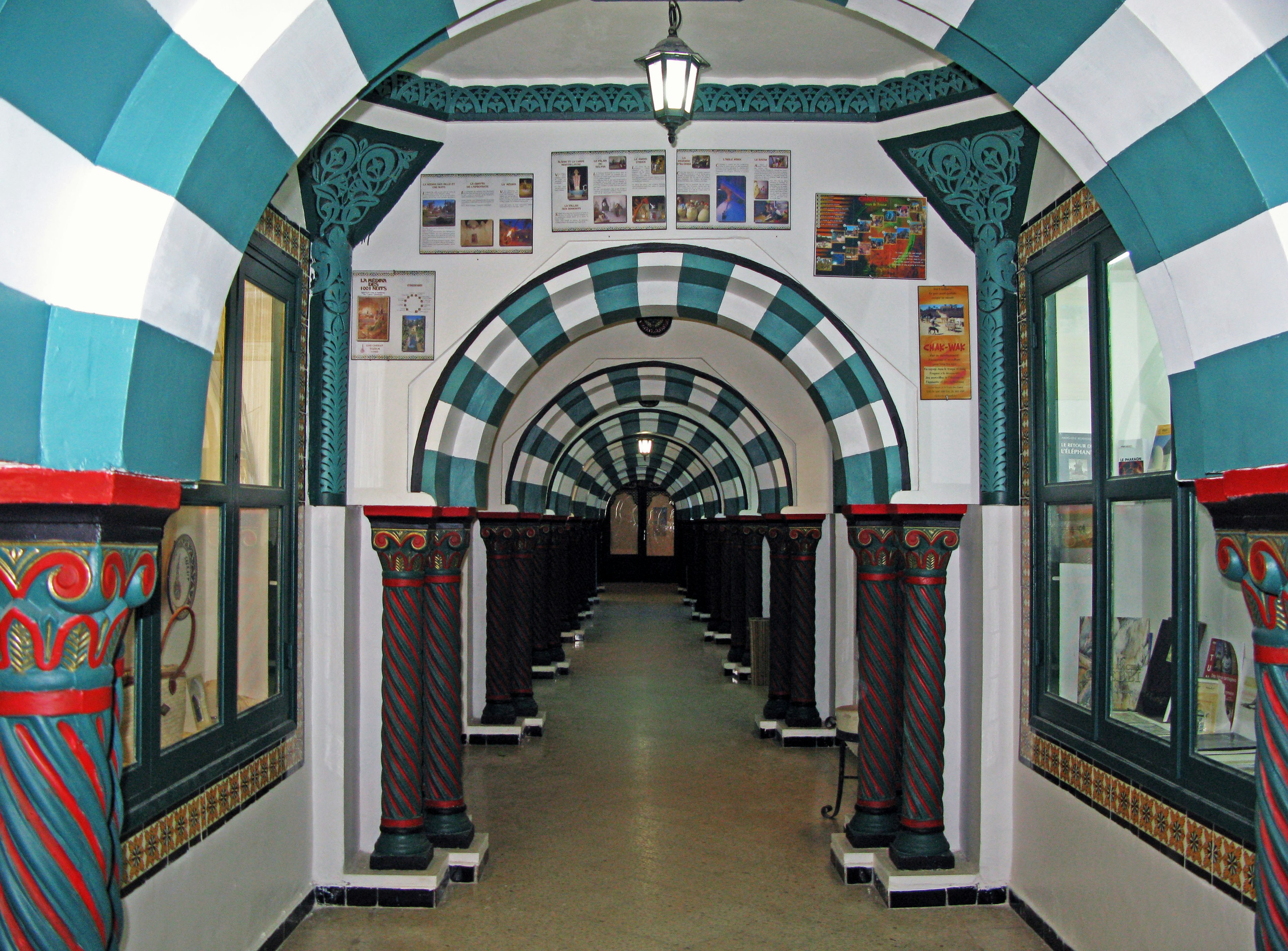 Un espacio interior con un pasillo arqueado a rayas azul y blanco, columnas decorativas y objetos en exhibición a ambos lados