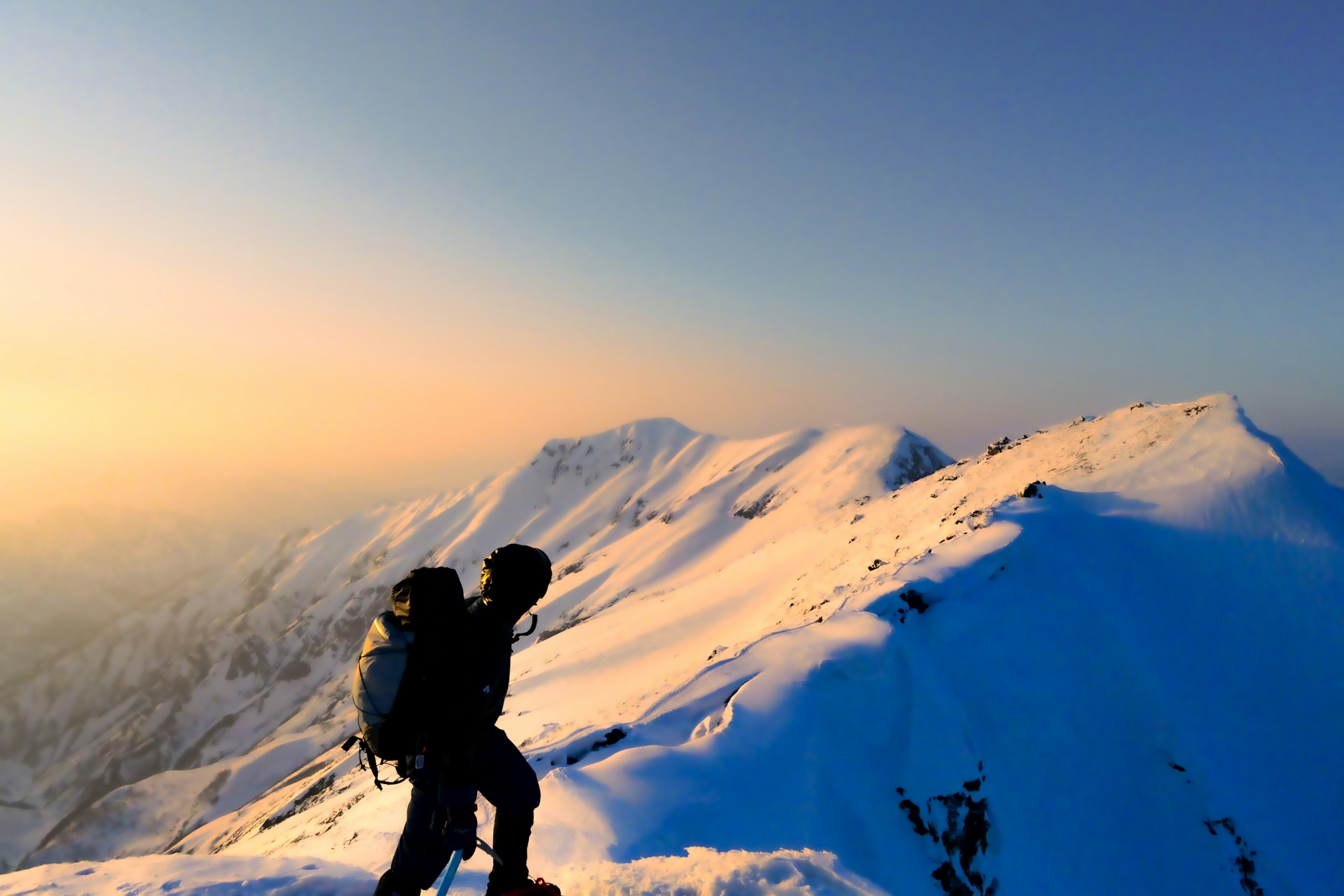 Hiker on a snowy mountain peak with sunset in the background