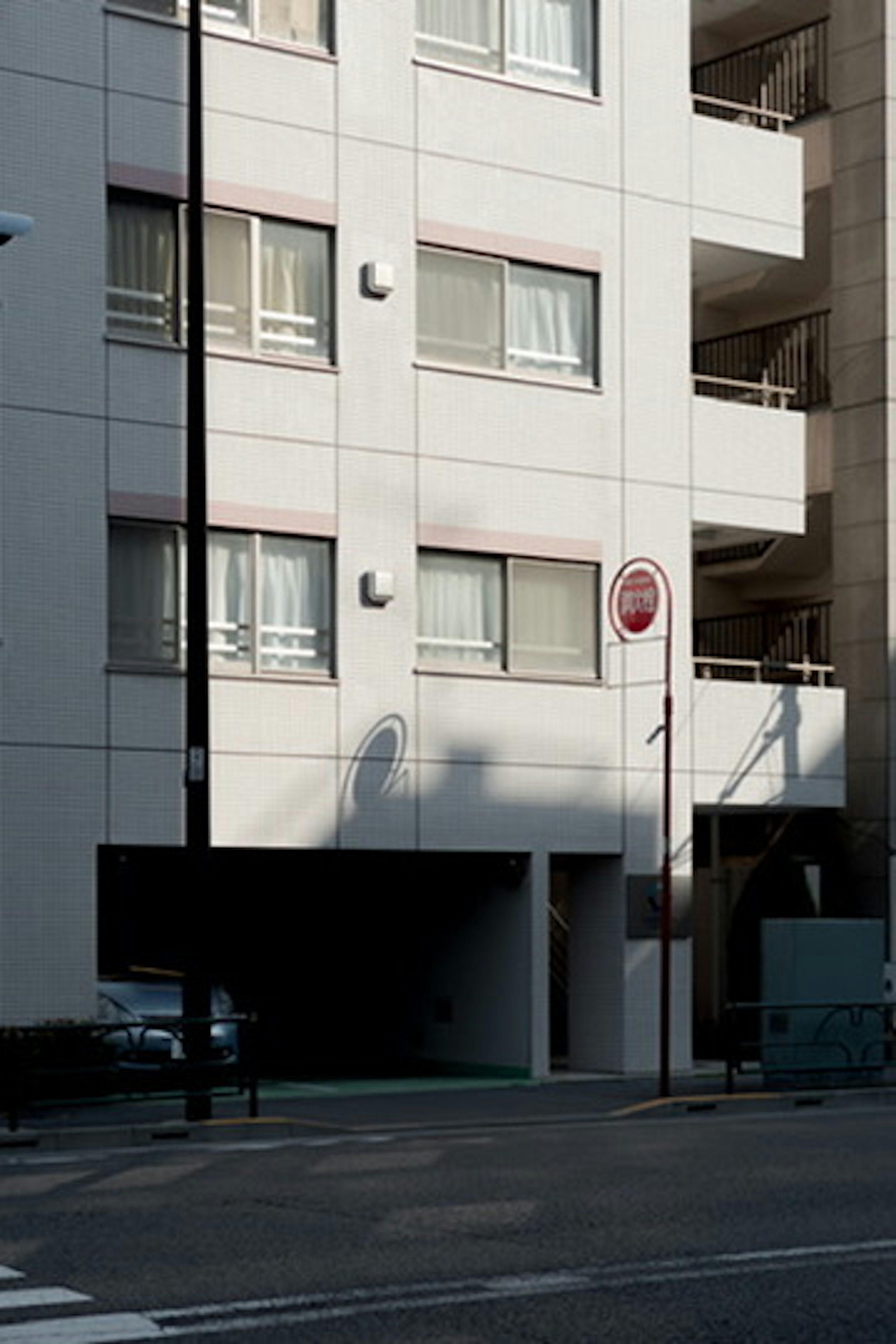 Vista de la calle que muestra un edificio blanco con ventanas visibles y un área de estacionamiento