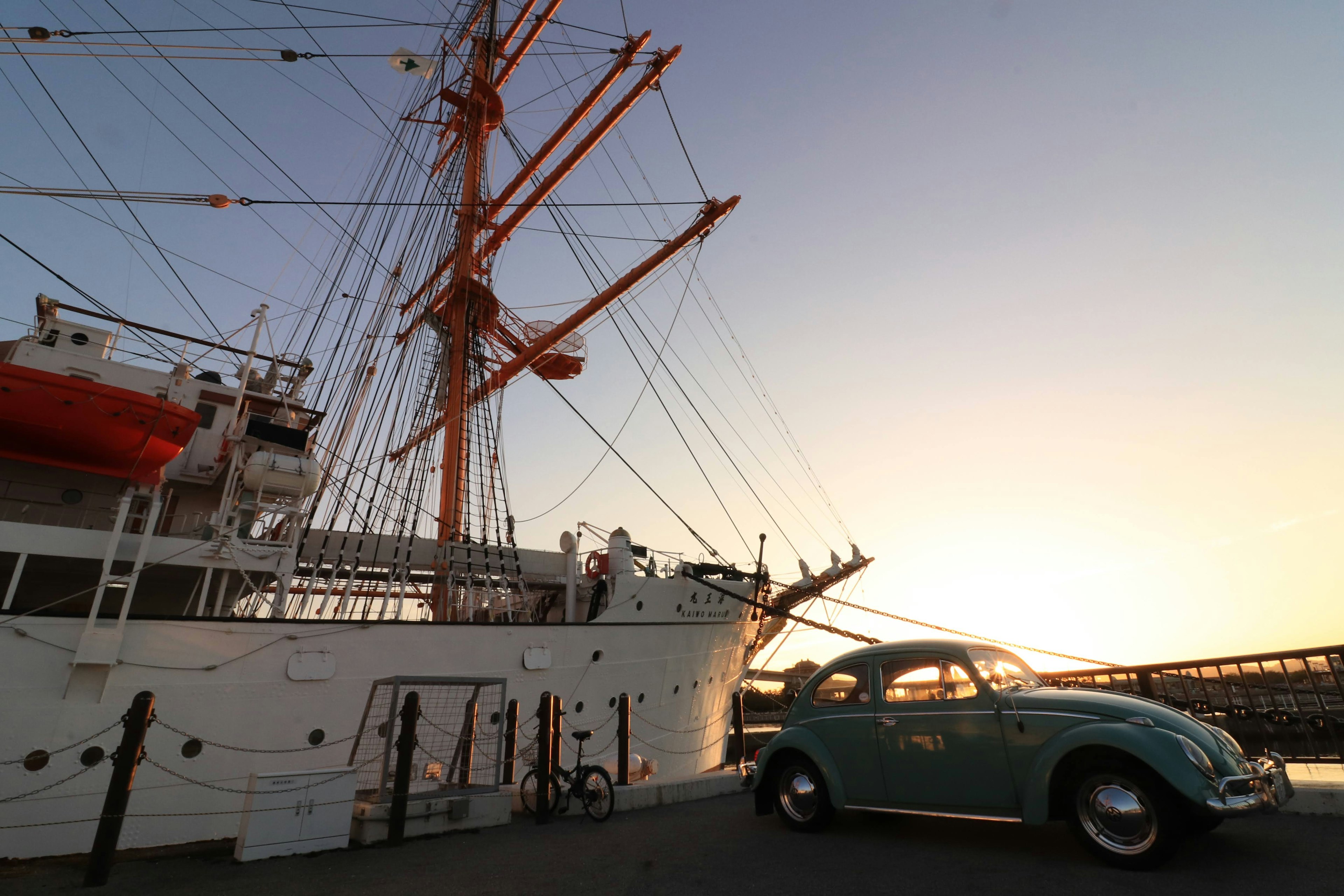 A ship docked at sunset with a vintage blue car