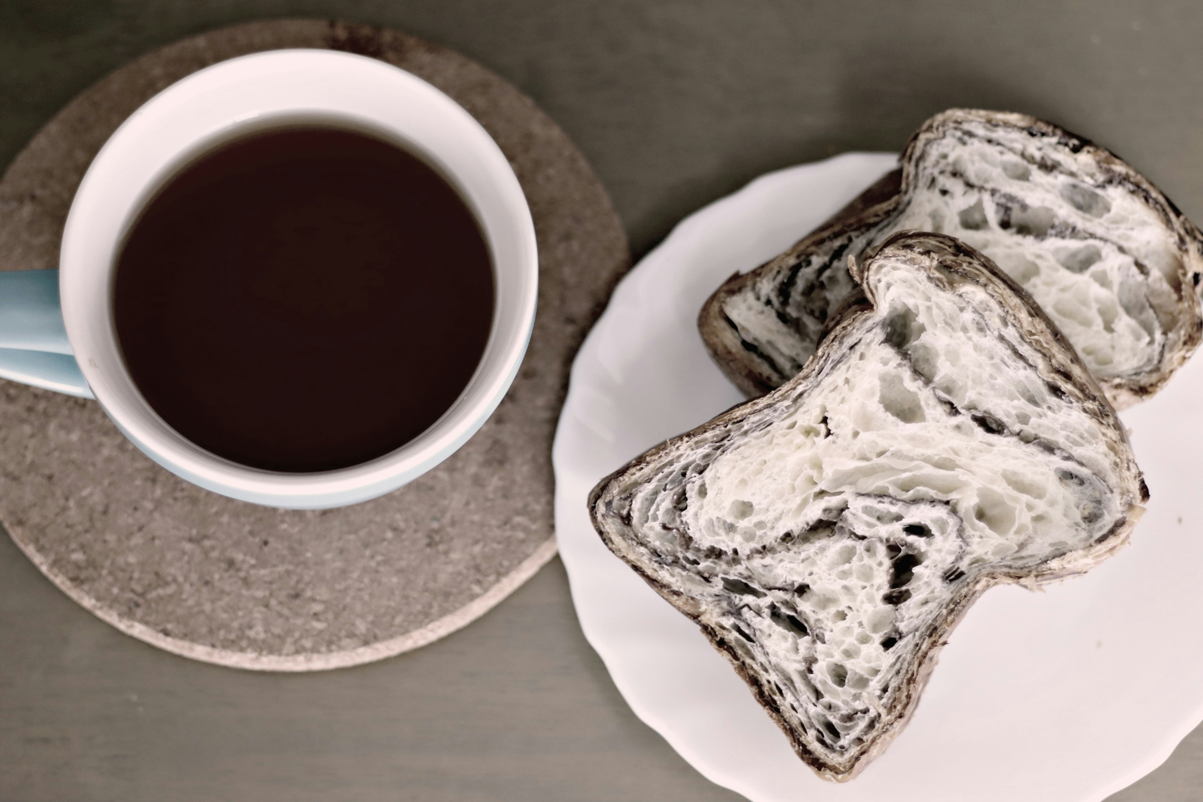 A cup of coffee beside slices of black sesame bread on a white plate