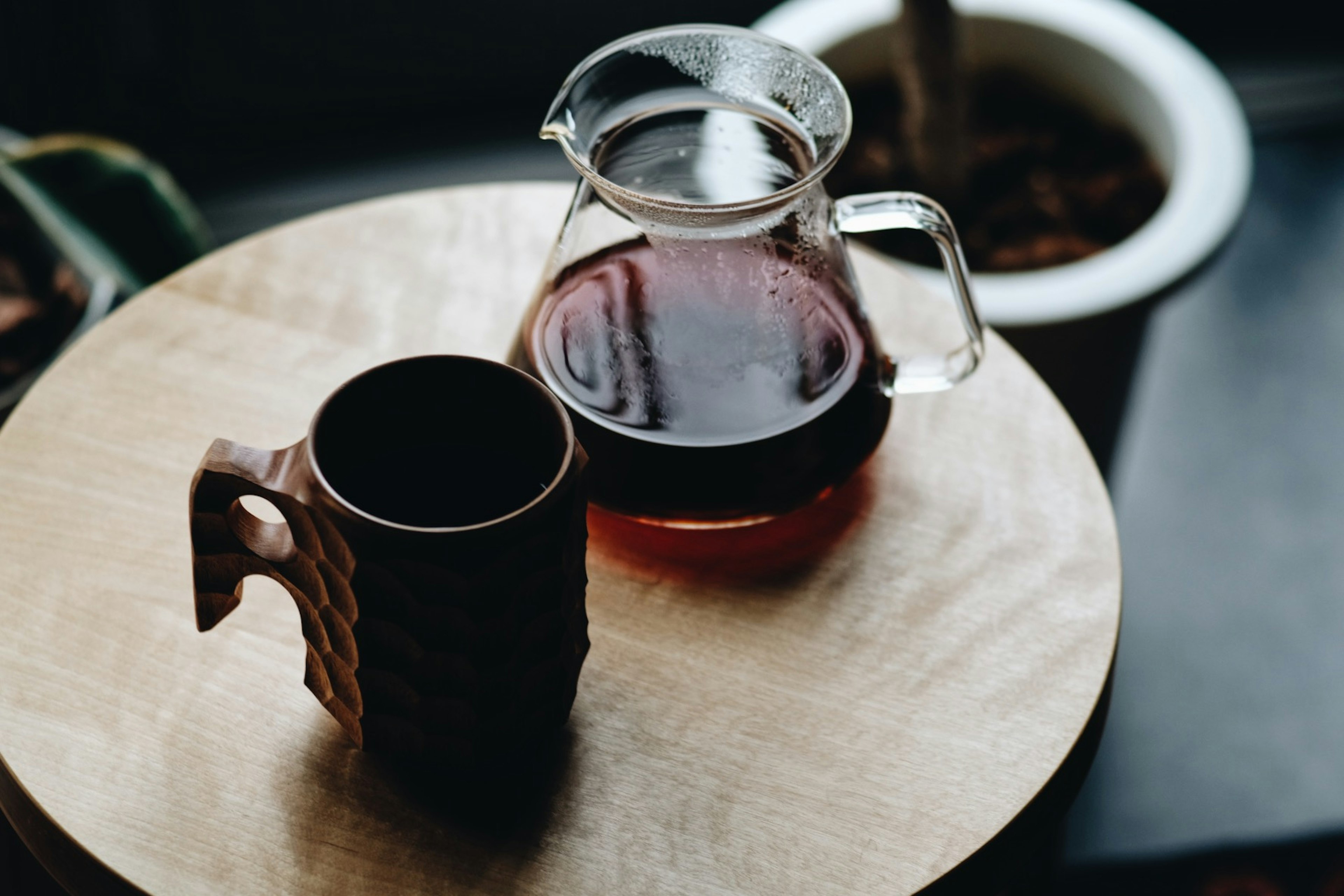 コーヒーの入ったガラスのポットと陶器のマグカップが木のトレイの上に置かれている