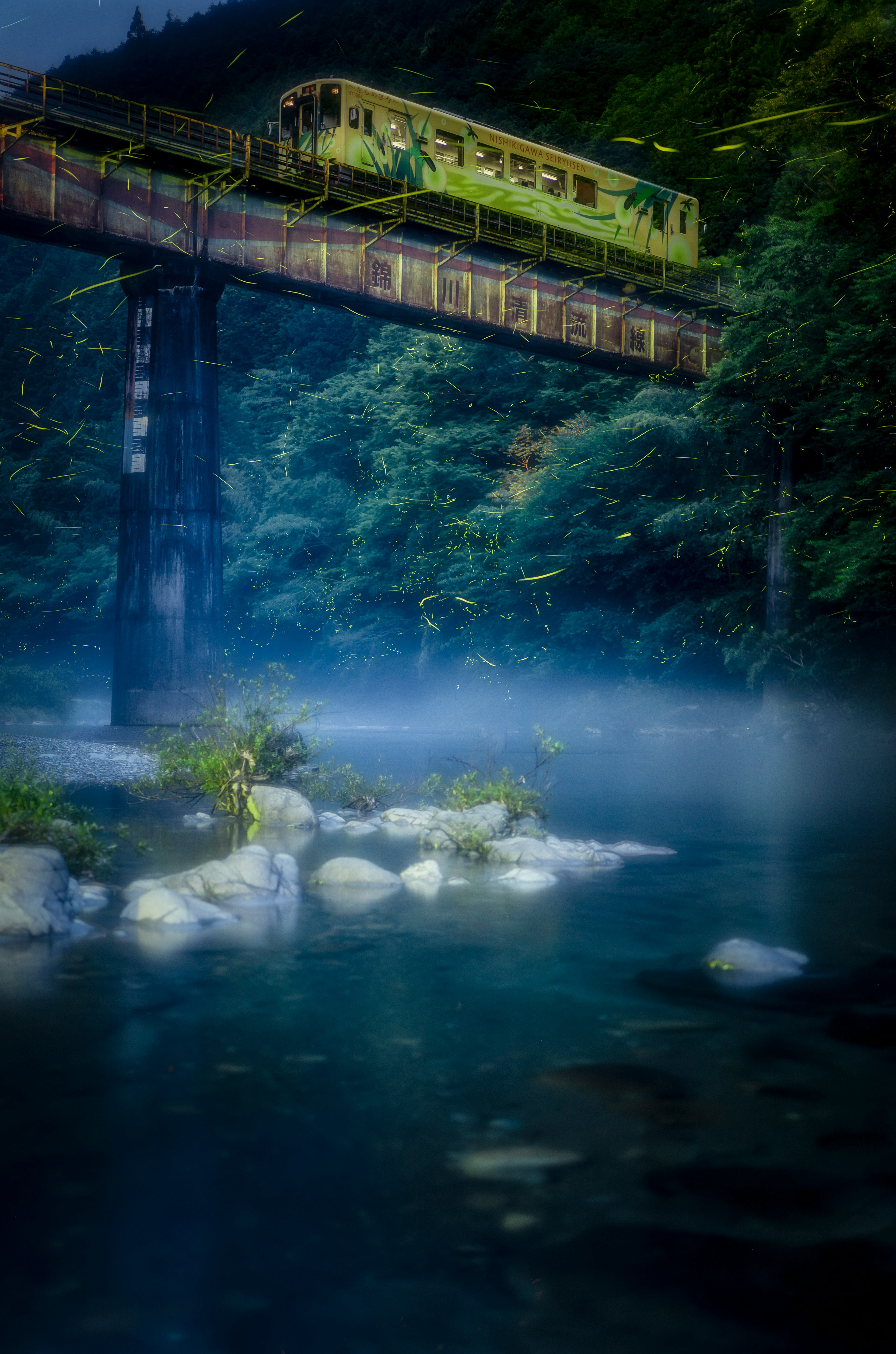 Un paysage d'une rivière avec de la brume bleue et un train vert sur un pont