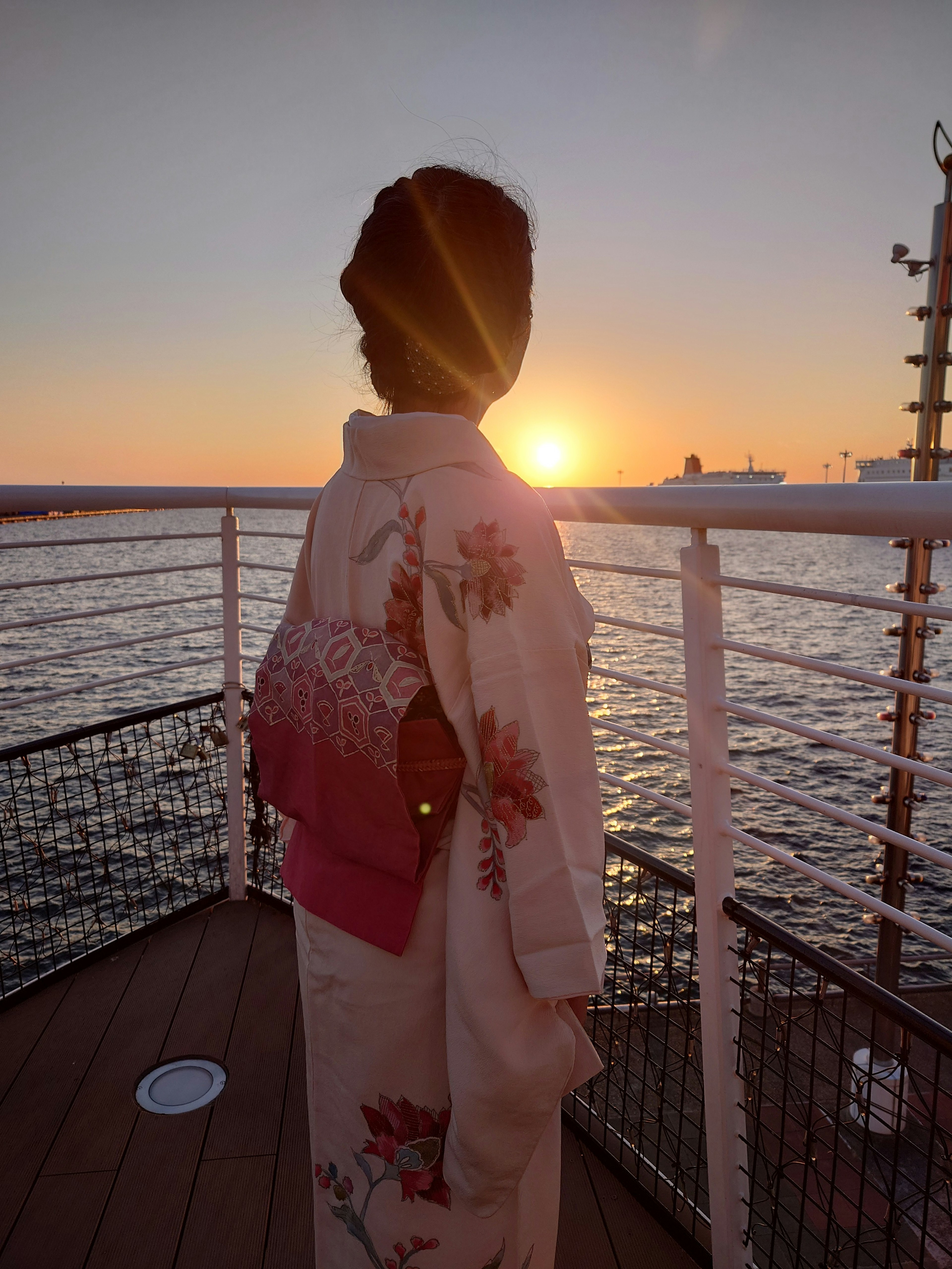 Eine Frau im Kimono, die auf das Meer mit dem Sonnenuntergang im Hintergrund schaut