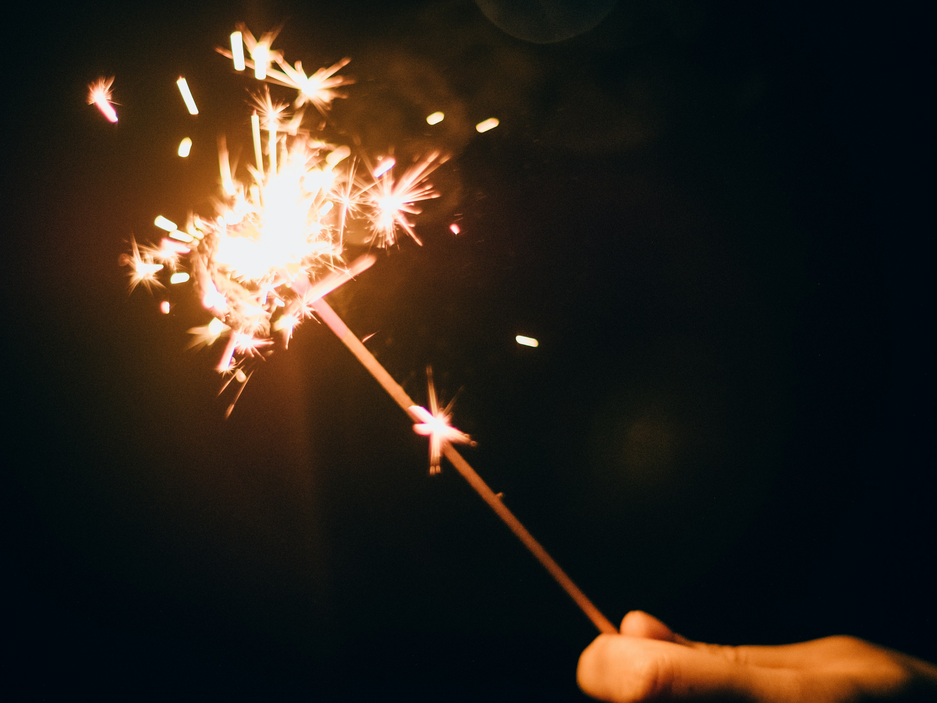 A hand holding a sparkler shining in the night sky