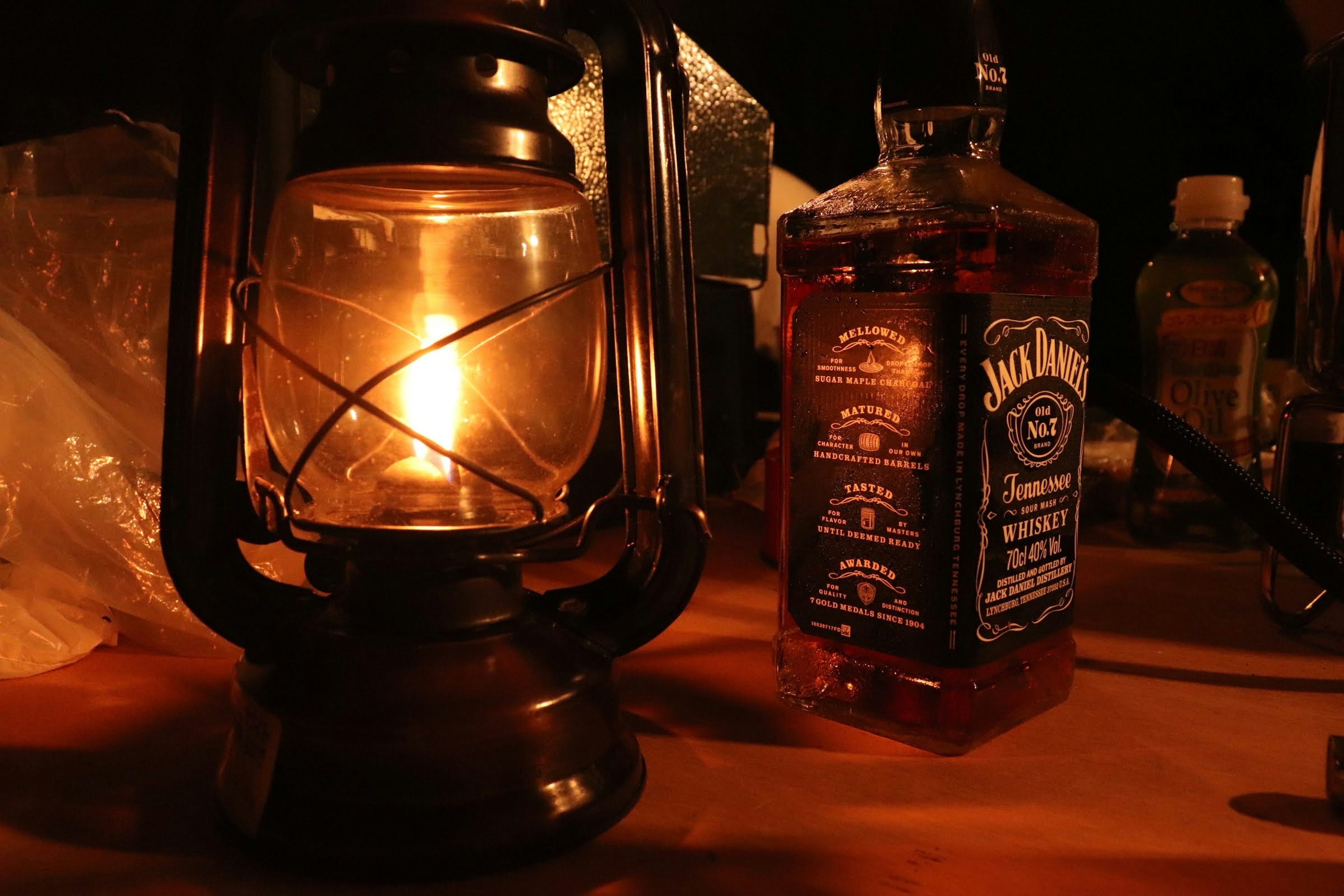 Image featuring a flickering oil lantern and a whiskey bottle against a dark background