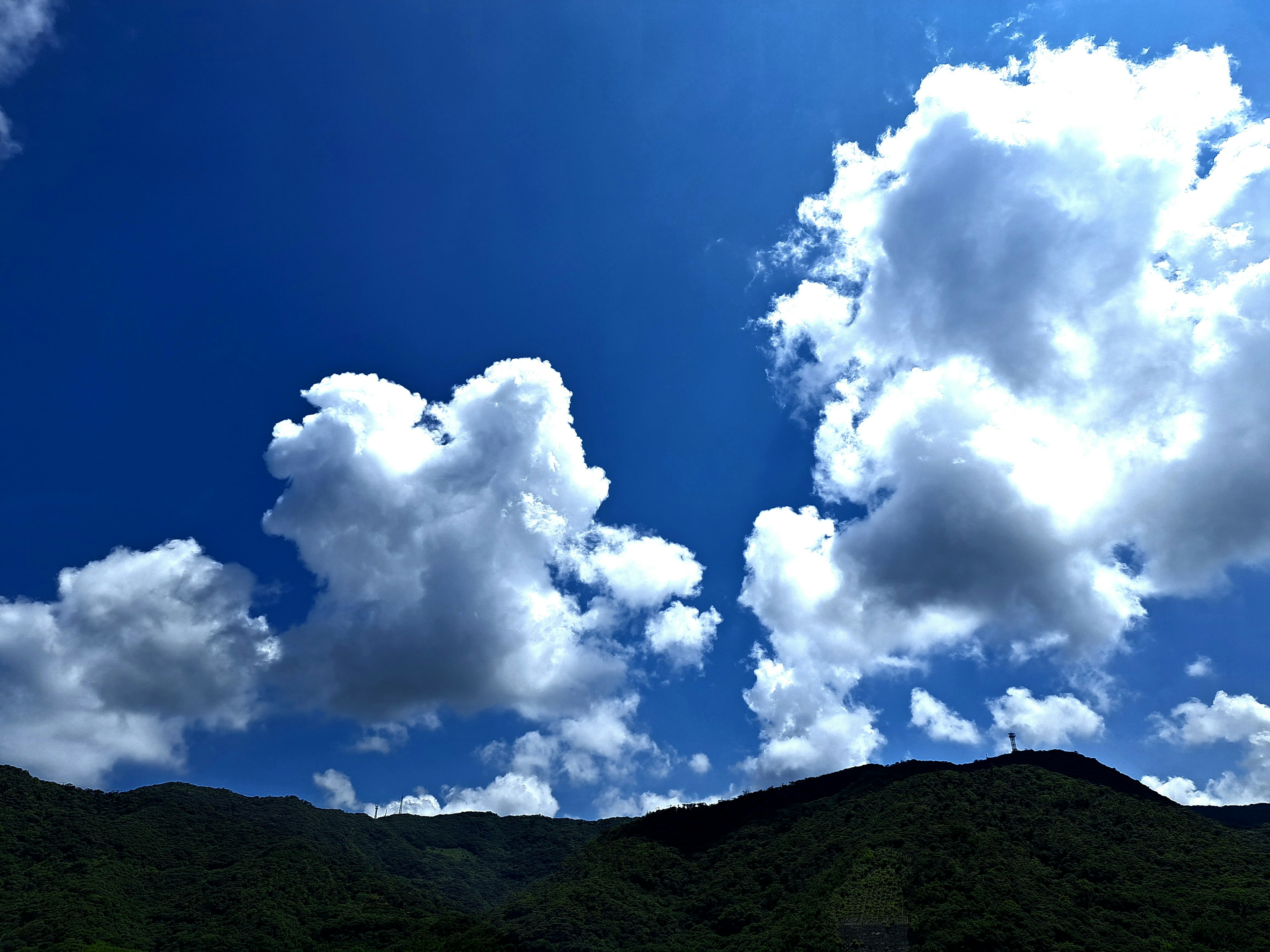 White clouds floating in a blue sky above green mountains