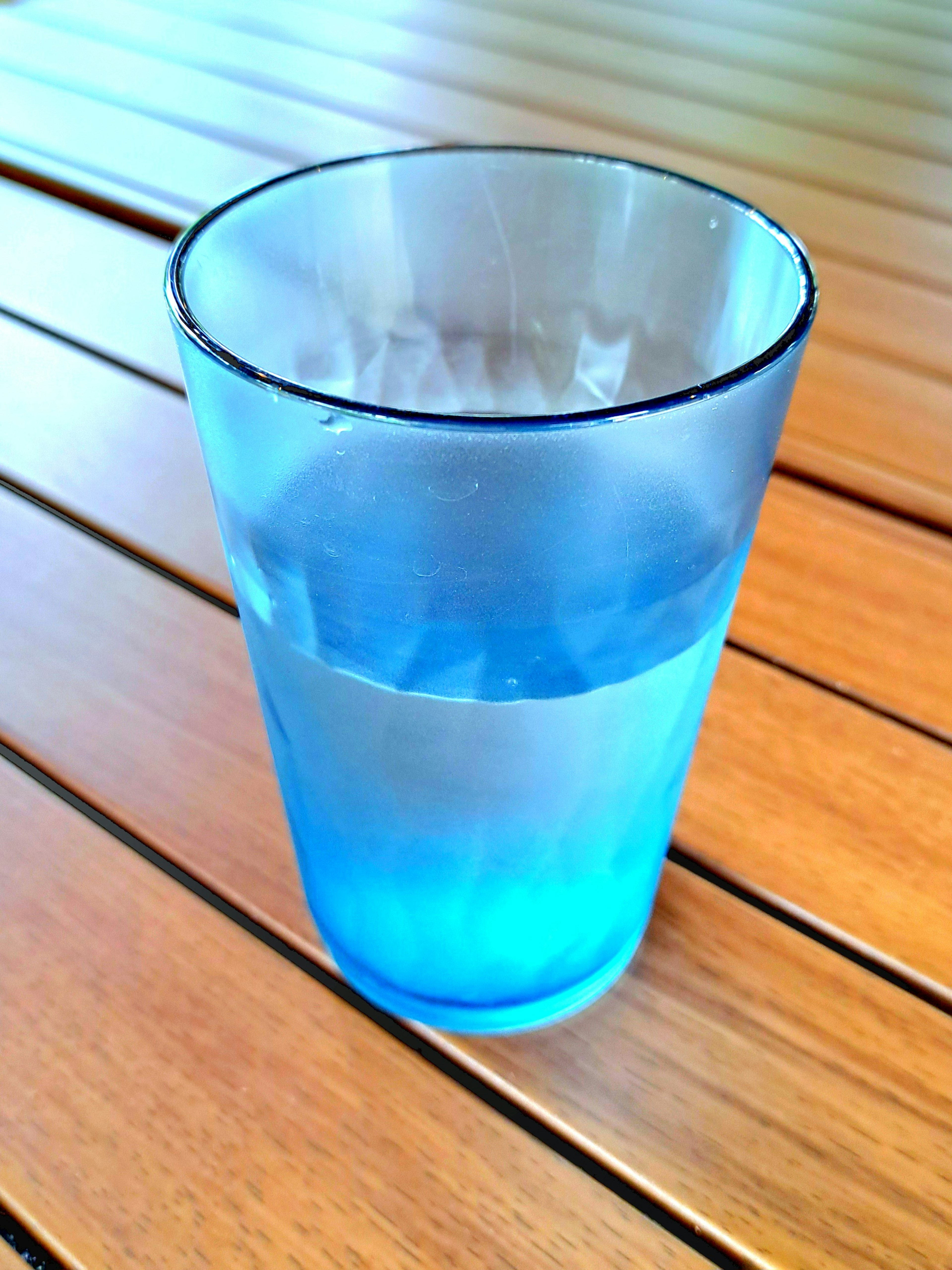 Gelas biru berisi air yang diletakkan di atas meja kayu