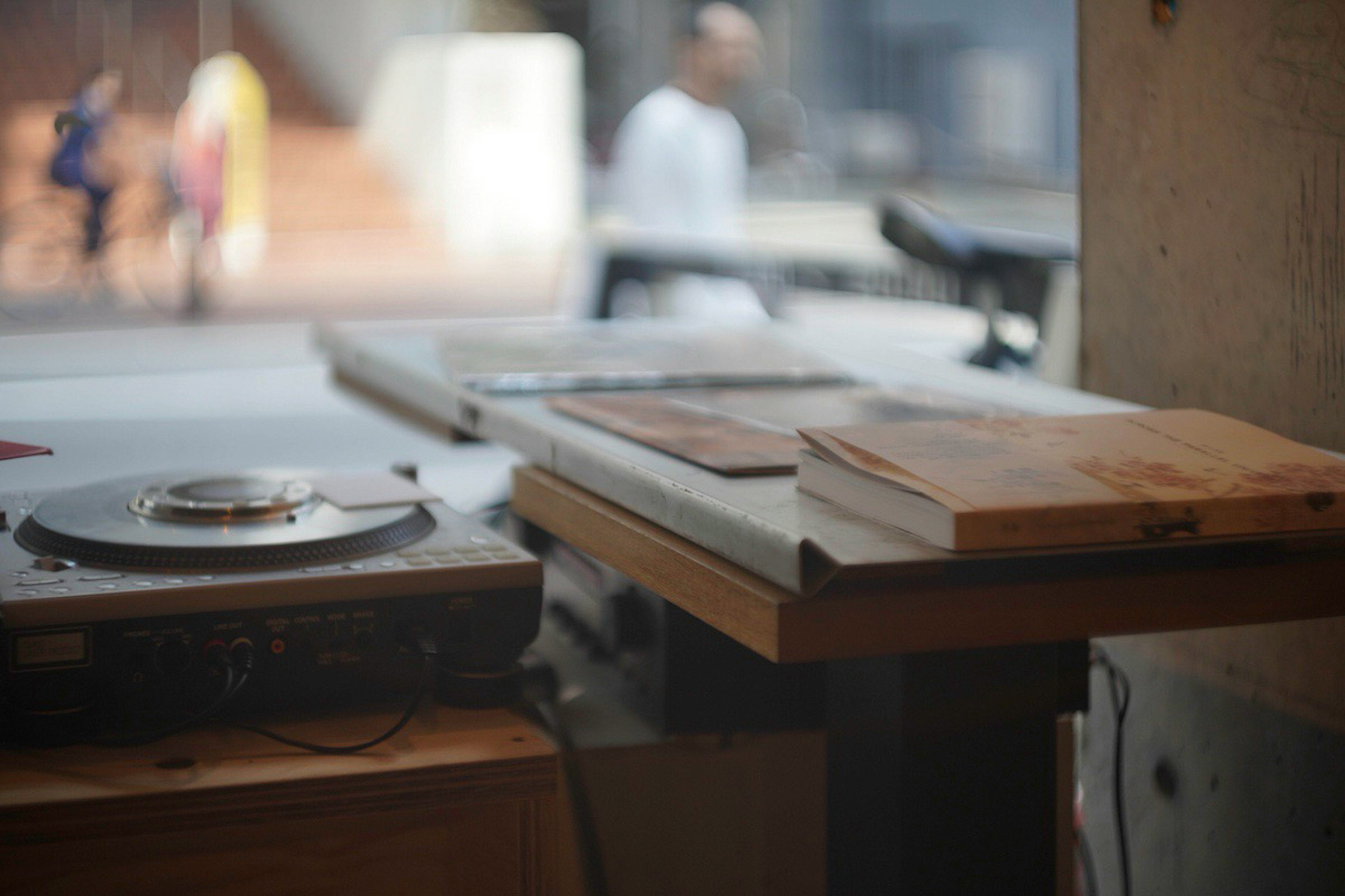 Sebuah turntable dan tumpukan buku di atas meja kayu dengan pejalan kaki buram di latar belakang