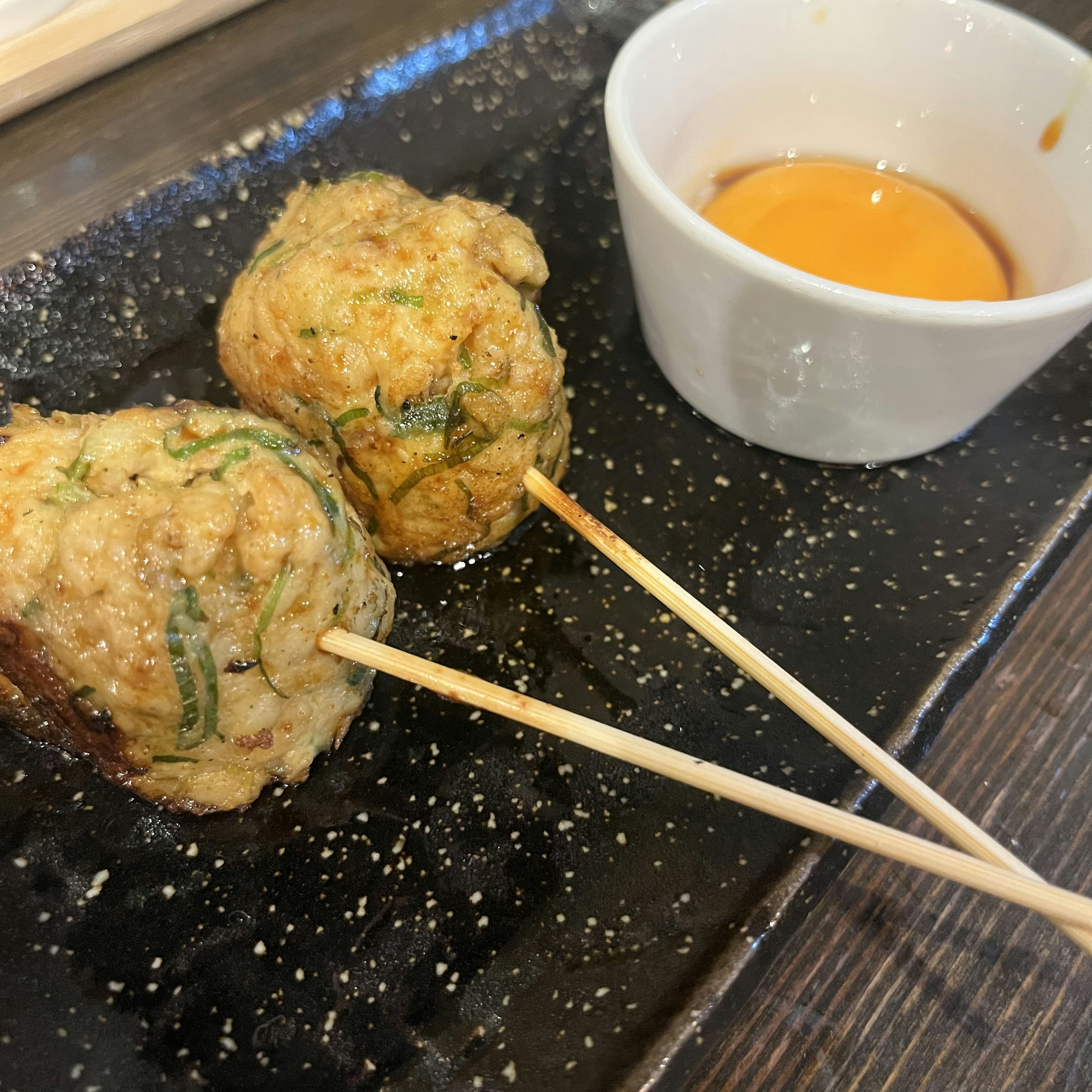 Two fried ball-shaped dishes on skewers served with a small white dipping sauce bowl