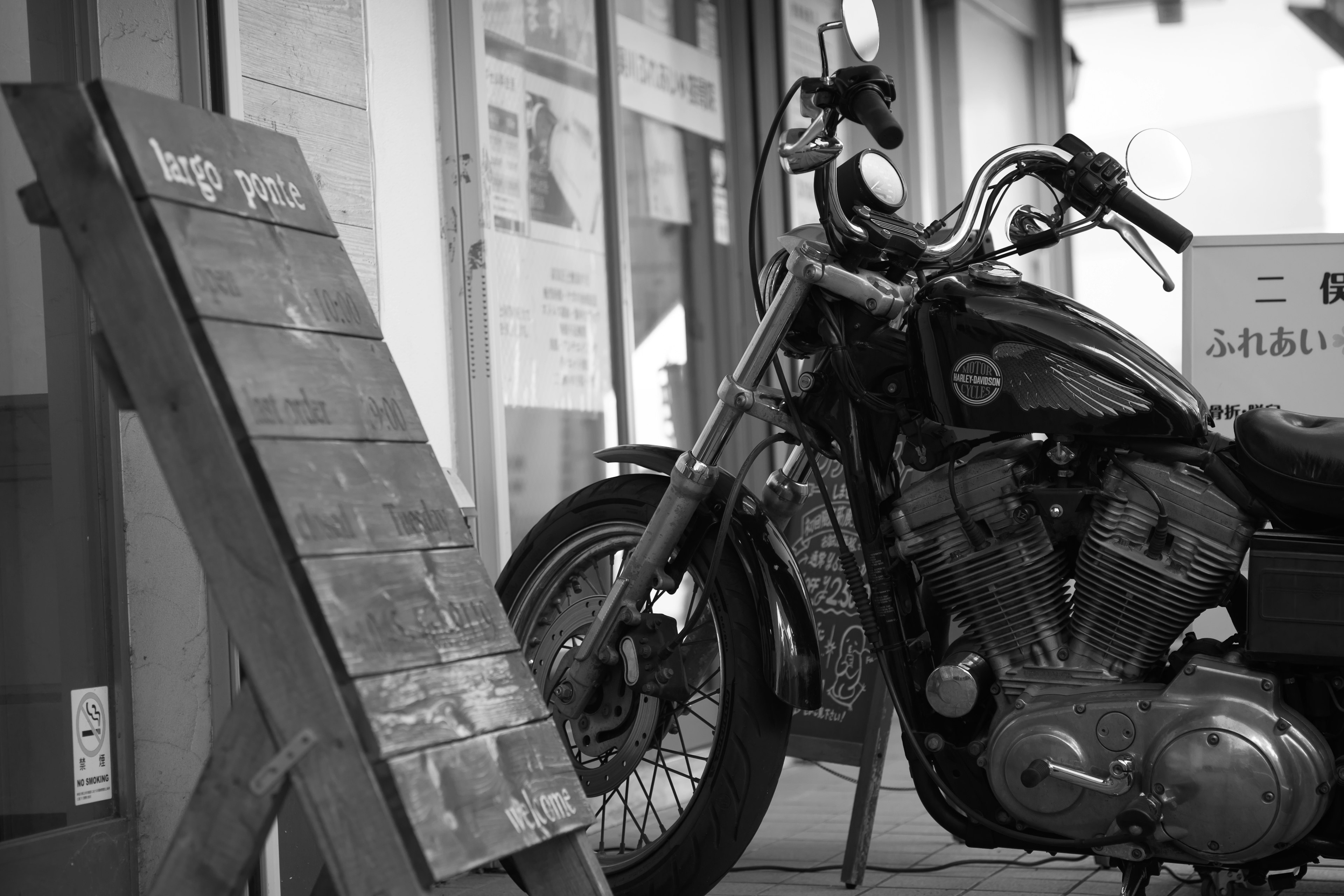 Motocicleta en blanco y negro estacionada junto a un cartel de madera