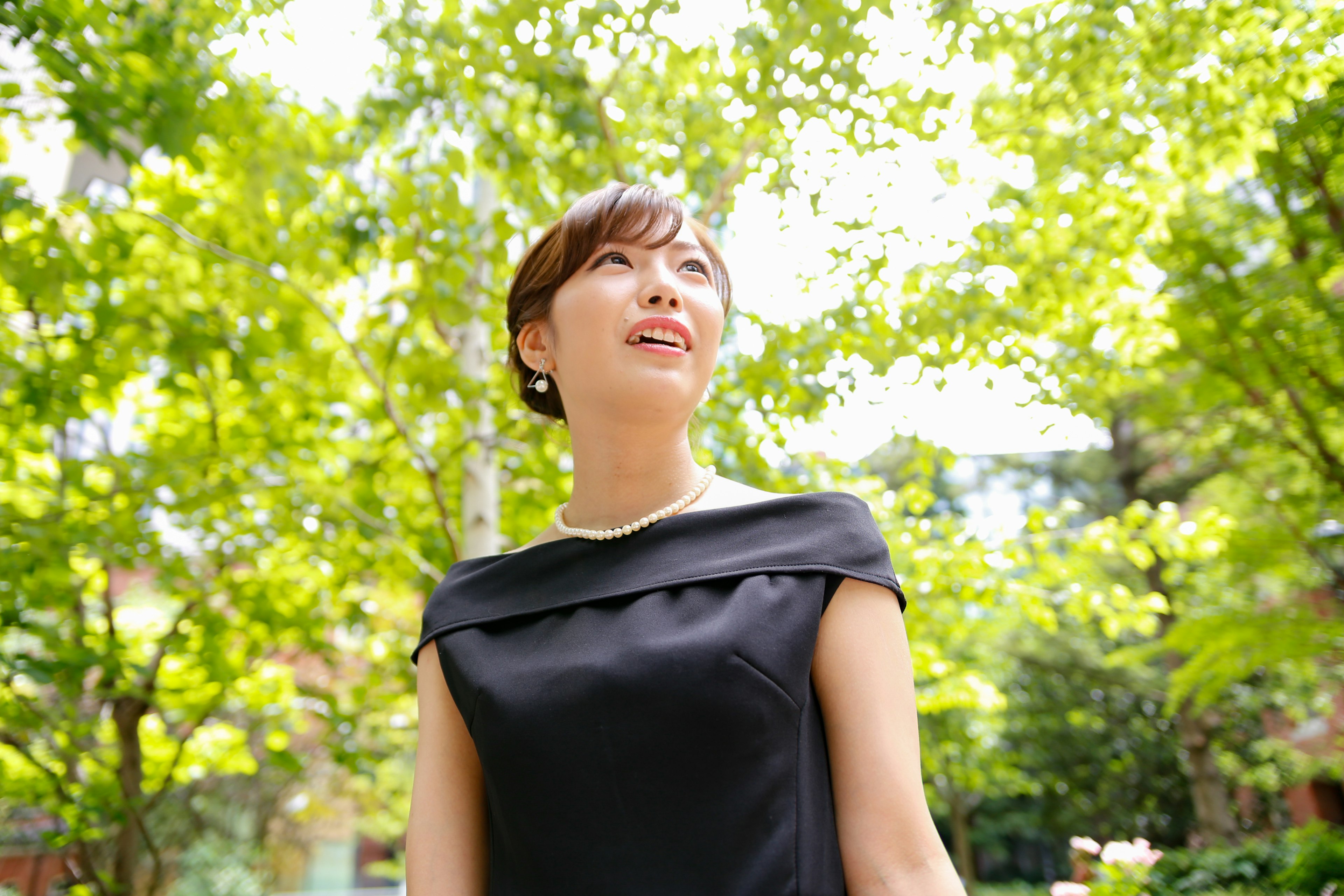 A woman in a black dress standing among green trees