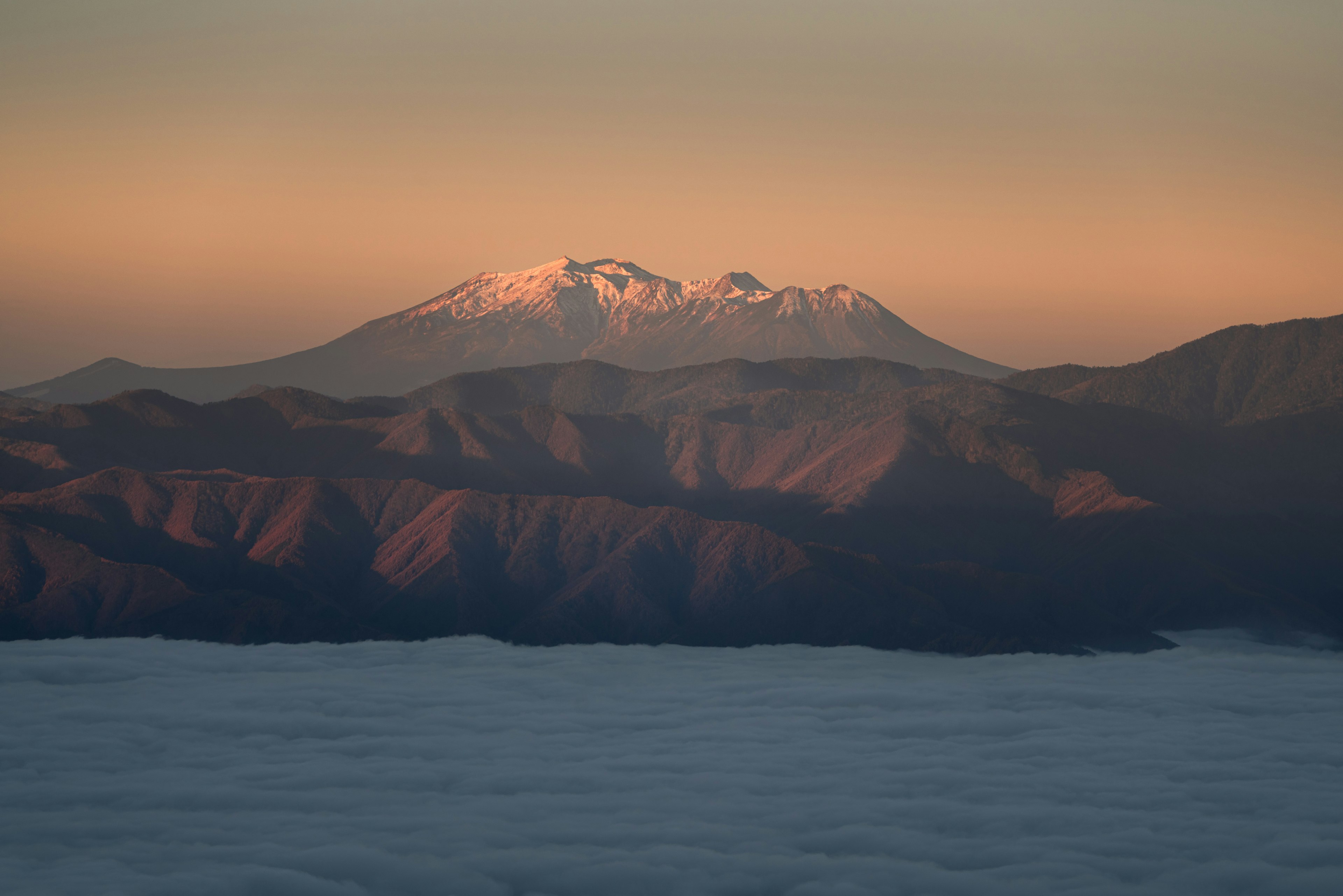 Lanskap pegunungan yang diterangi matahari terbenam dengan puncak bersalju