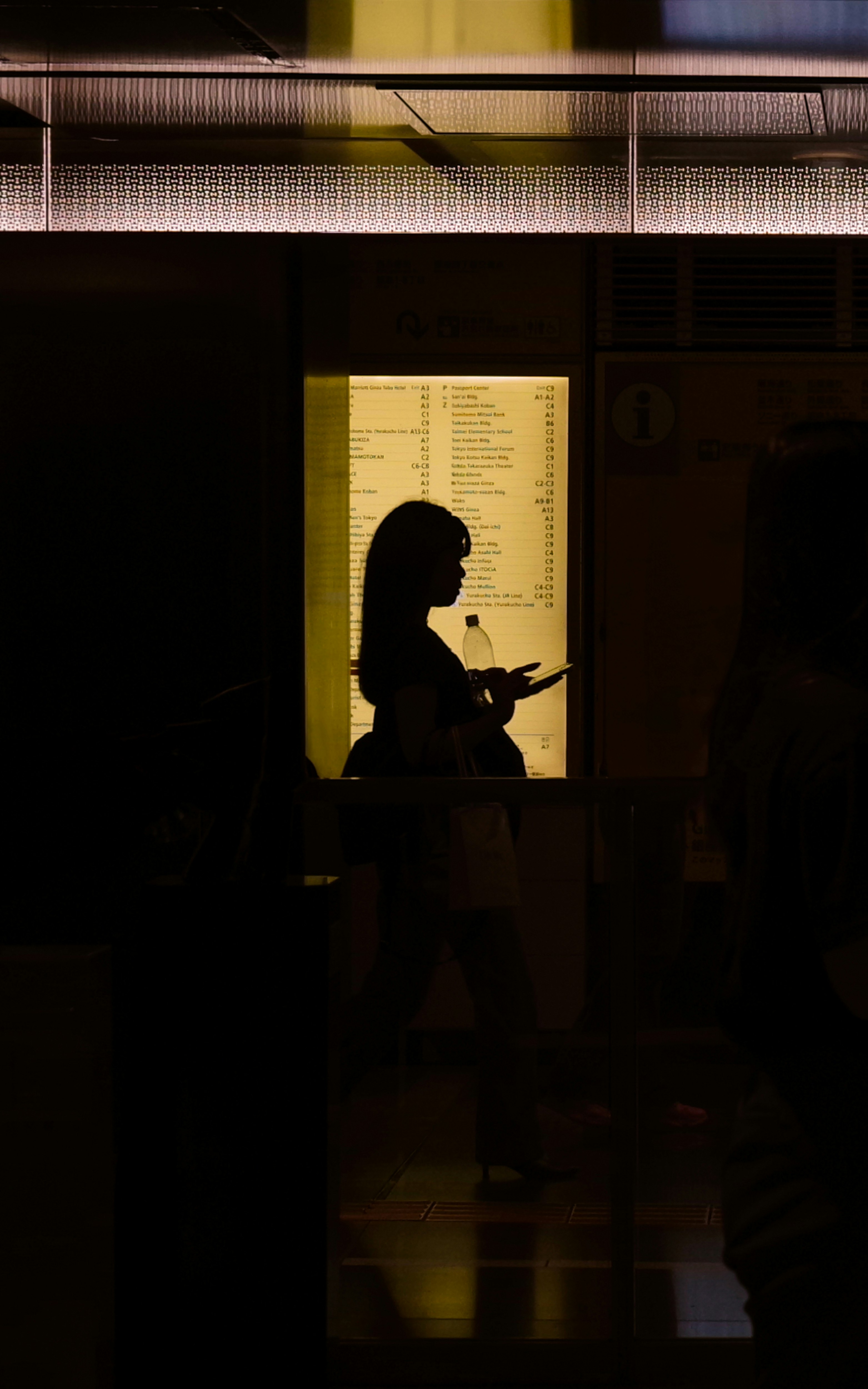 Silhouette of a woman holding a smartphone in front of a bright yellow light