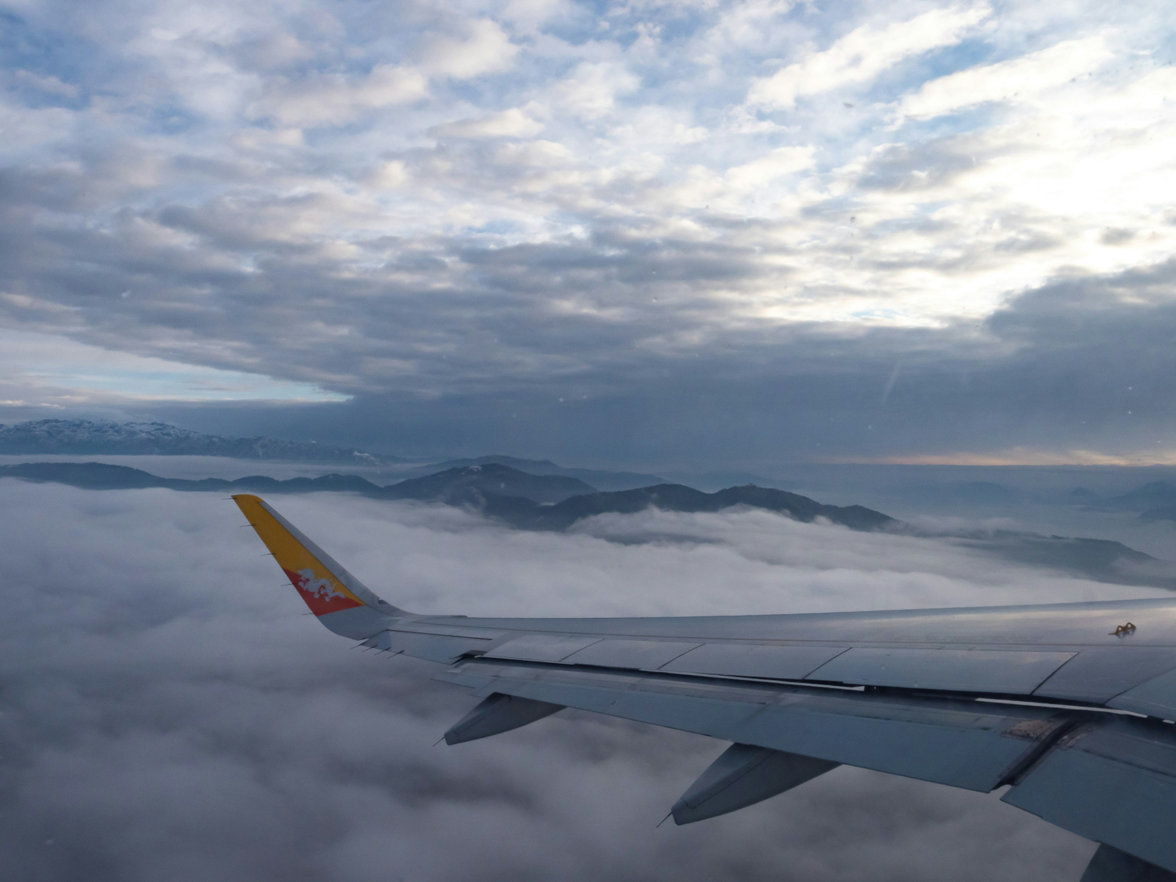 Pemandangan pegunungan di atas awan dengan sayap pesawat