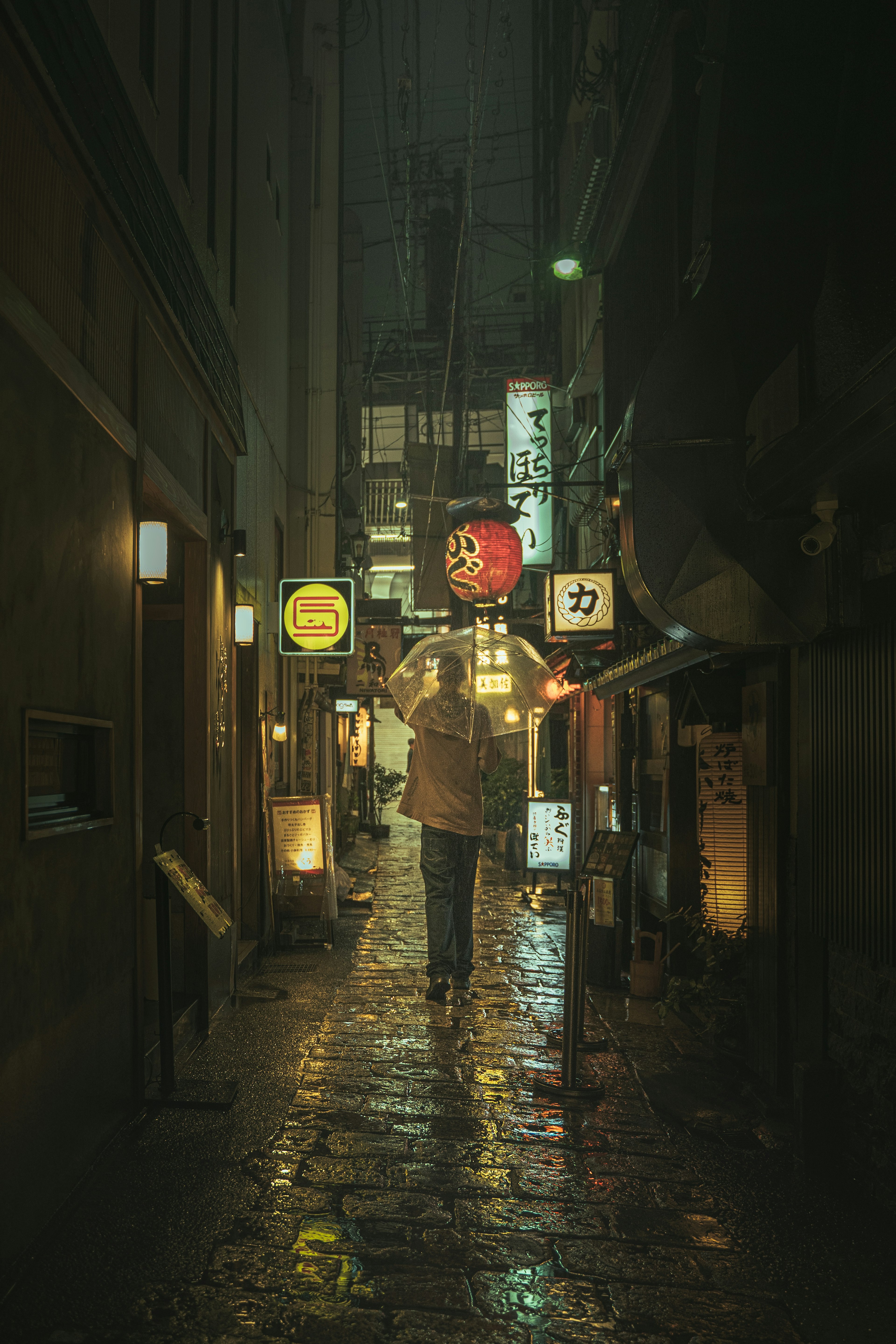 Una persona caminando en un callejón lluvioso con letreros de neón por la noche