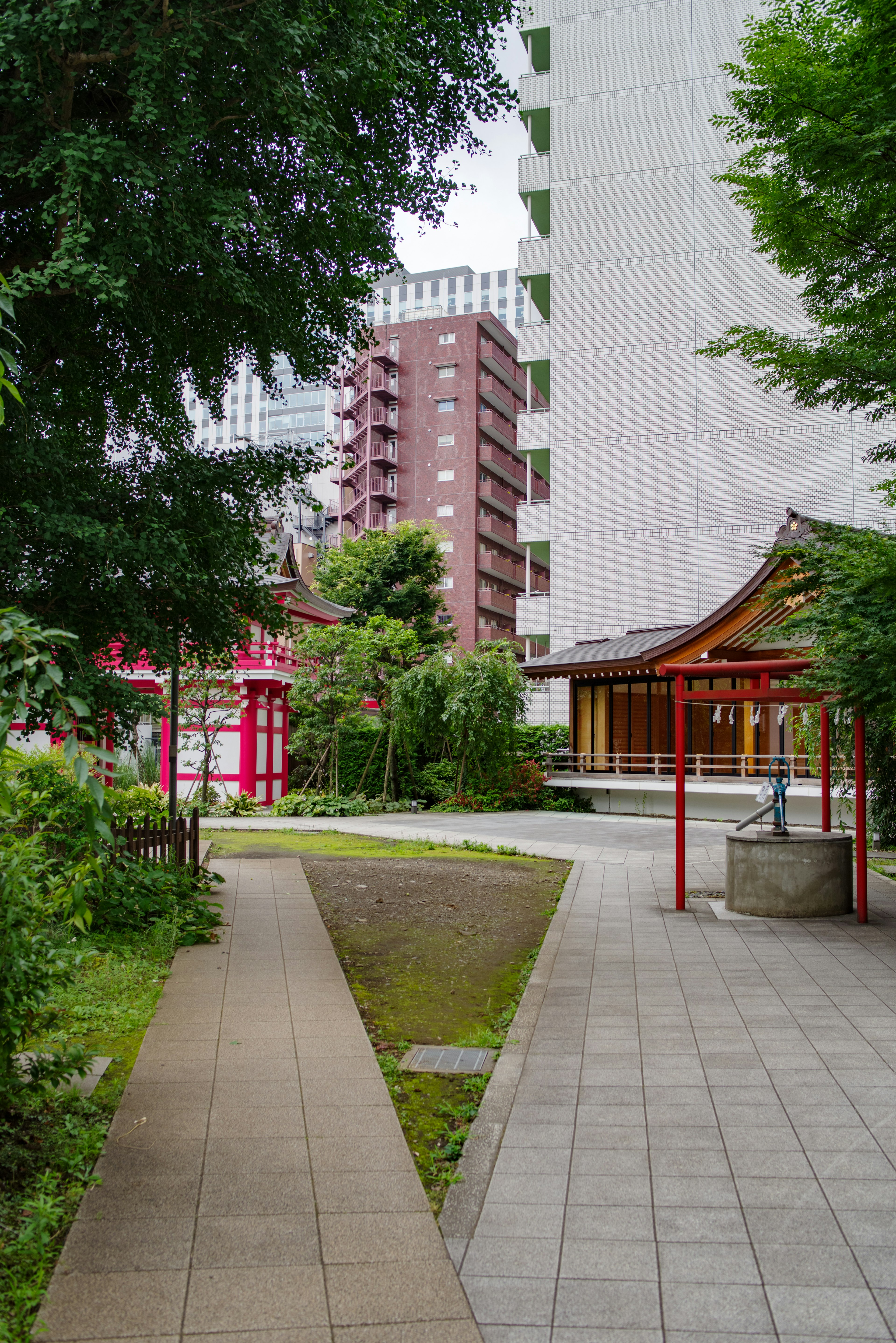 A serene park pathway surrounded by greenery and a traditional shrine building