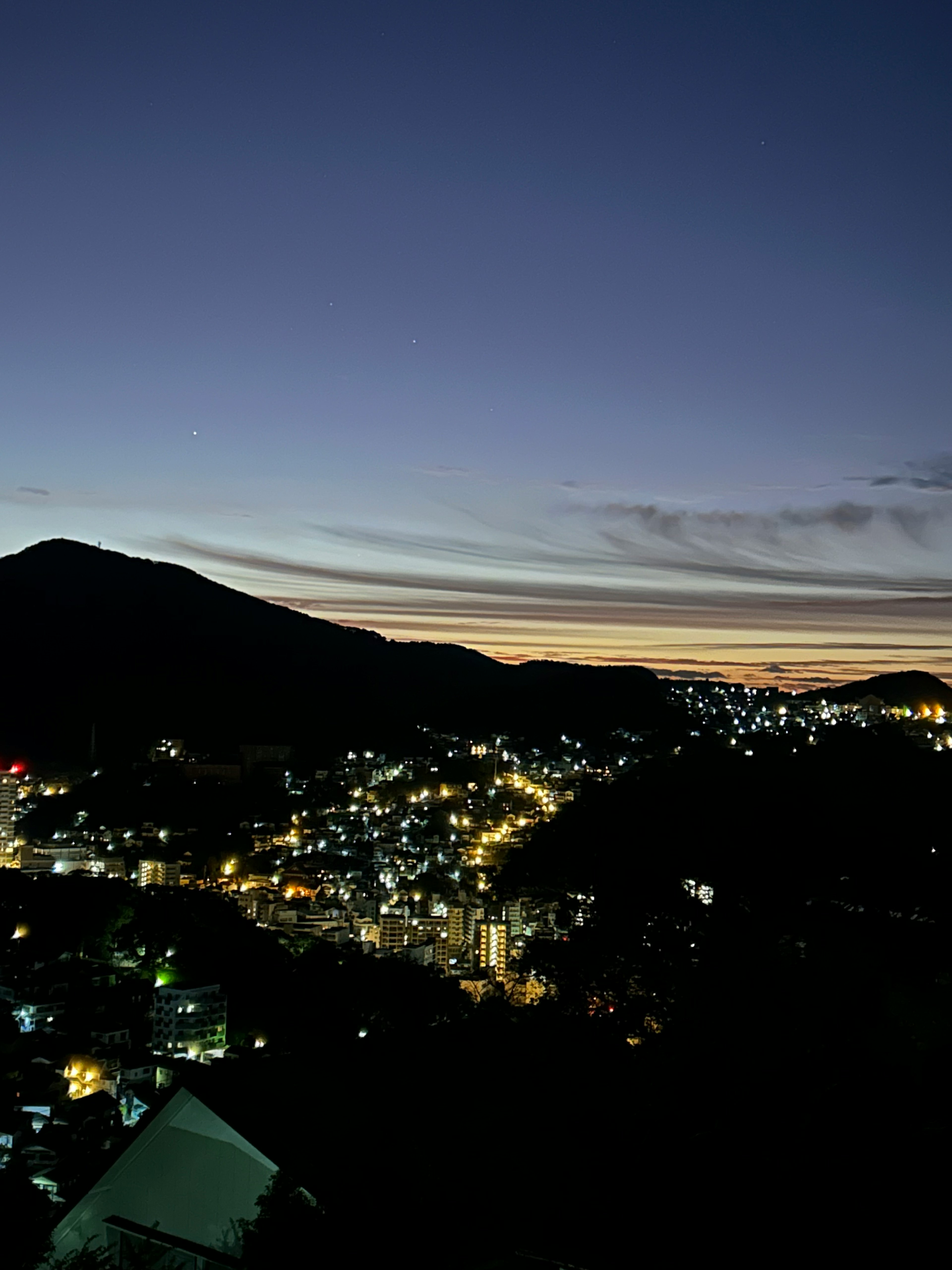 Vista notturna di una città con luci brillanti e silhouette di montagna