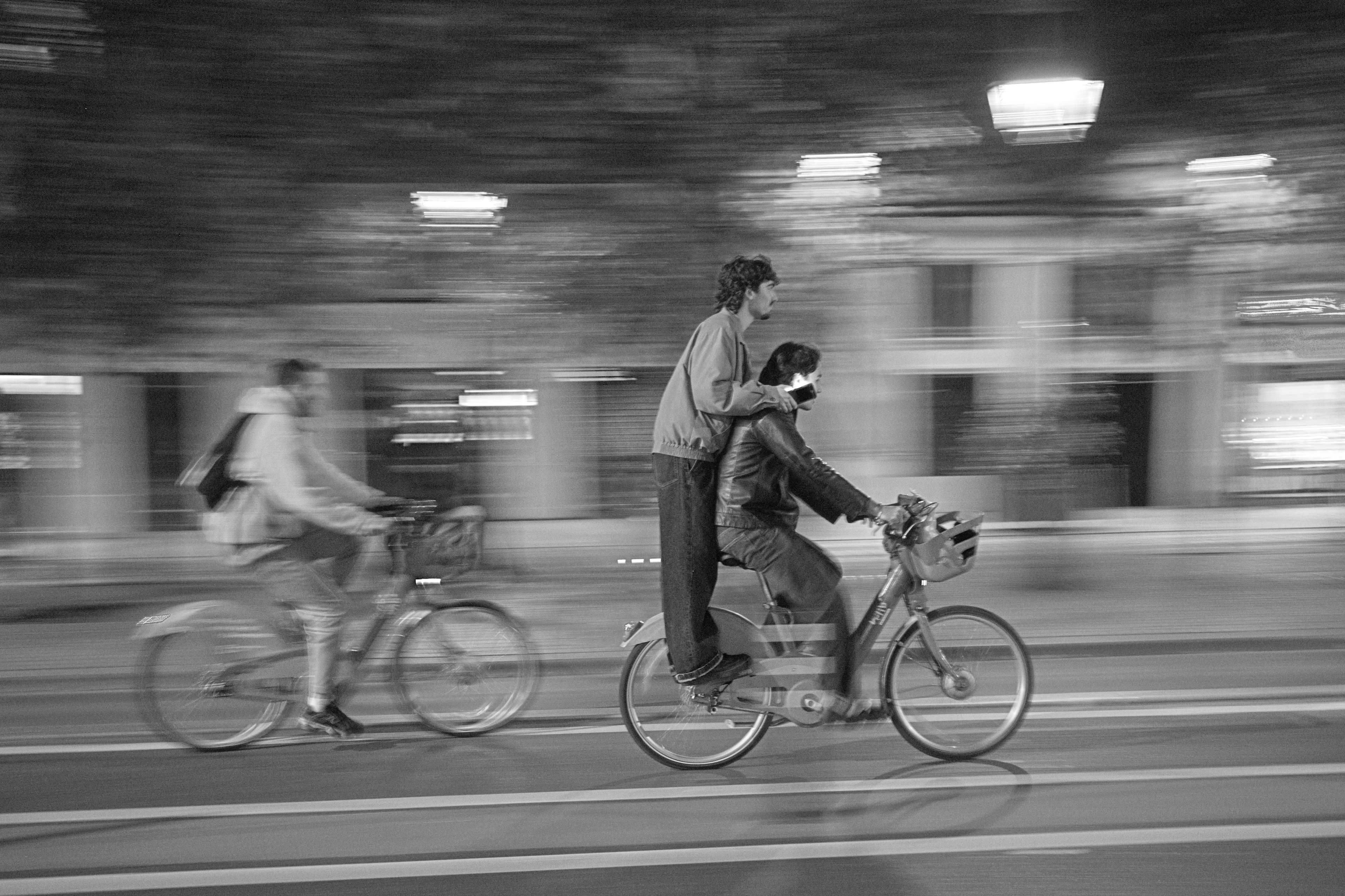 Two people riding a bicycle in a city at night with motion blur