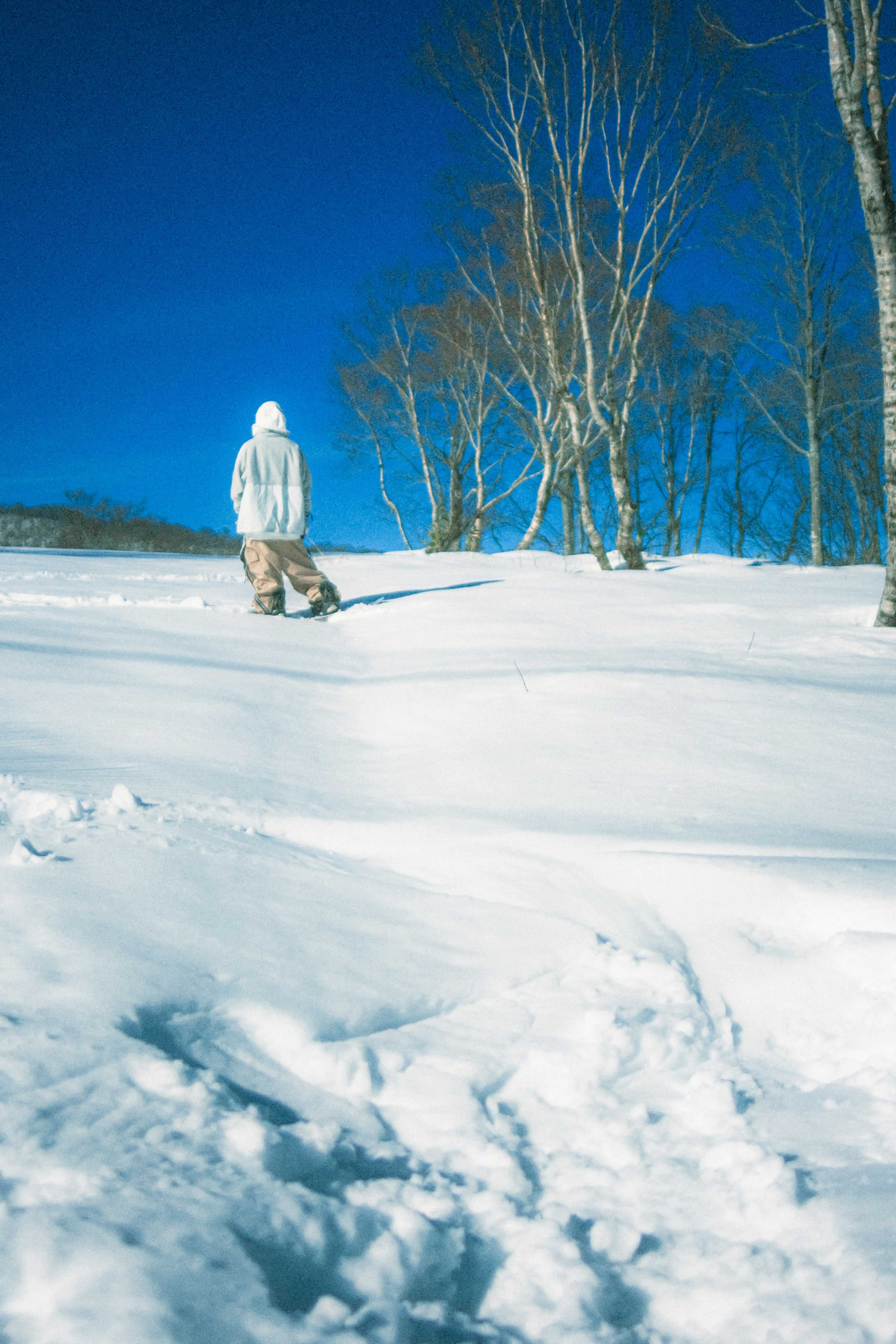 Personne marchant dans un paysage enneigé vêtue de blanc sous un ciel bleu