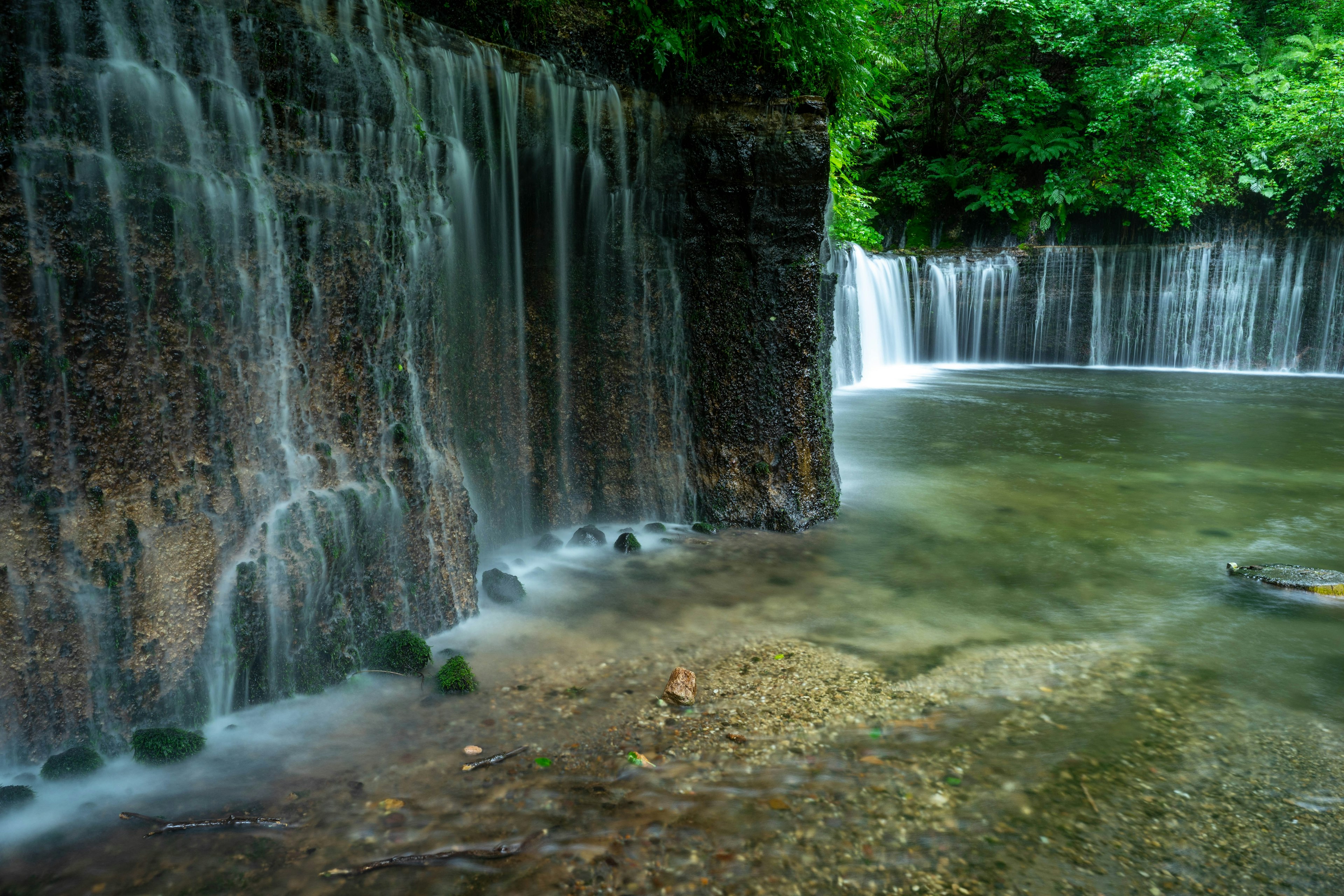 Air terjun tenang dikelilingi oleh pepohonan rimbun dengan air jernih