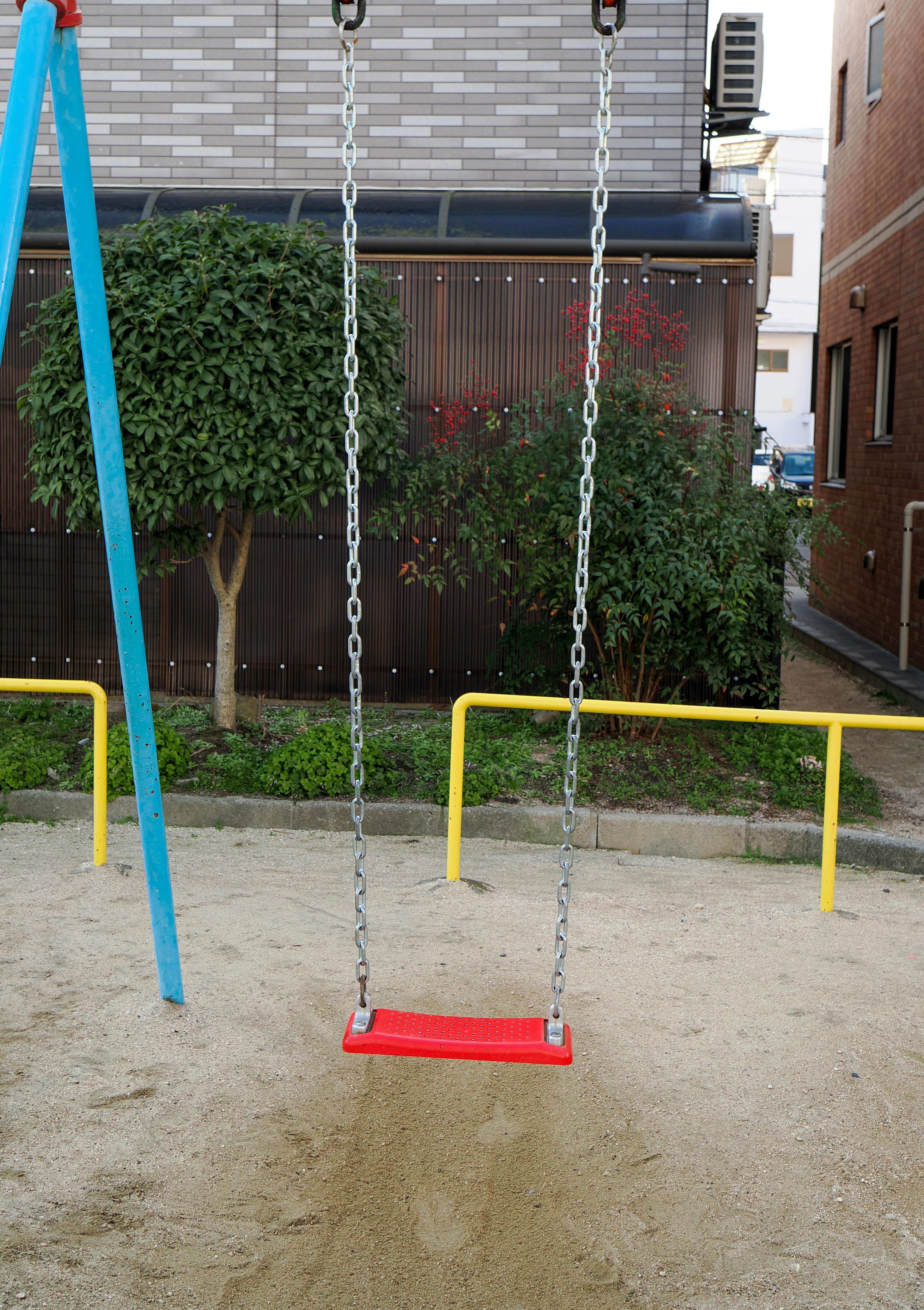 Parque infantil sencillo con un columpio rojo y un poste de soporte azul