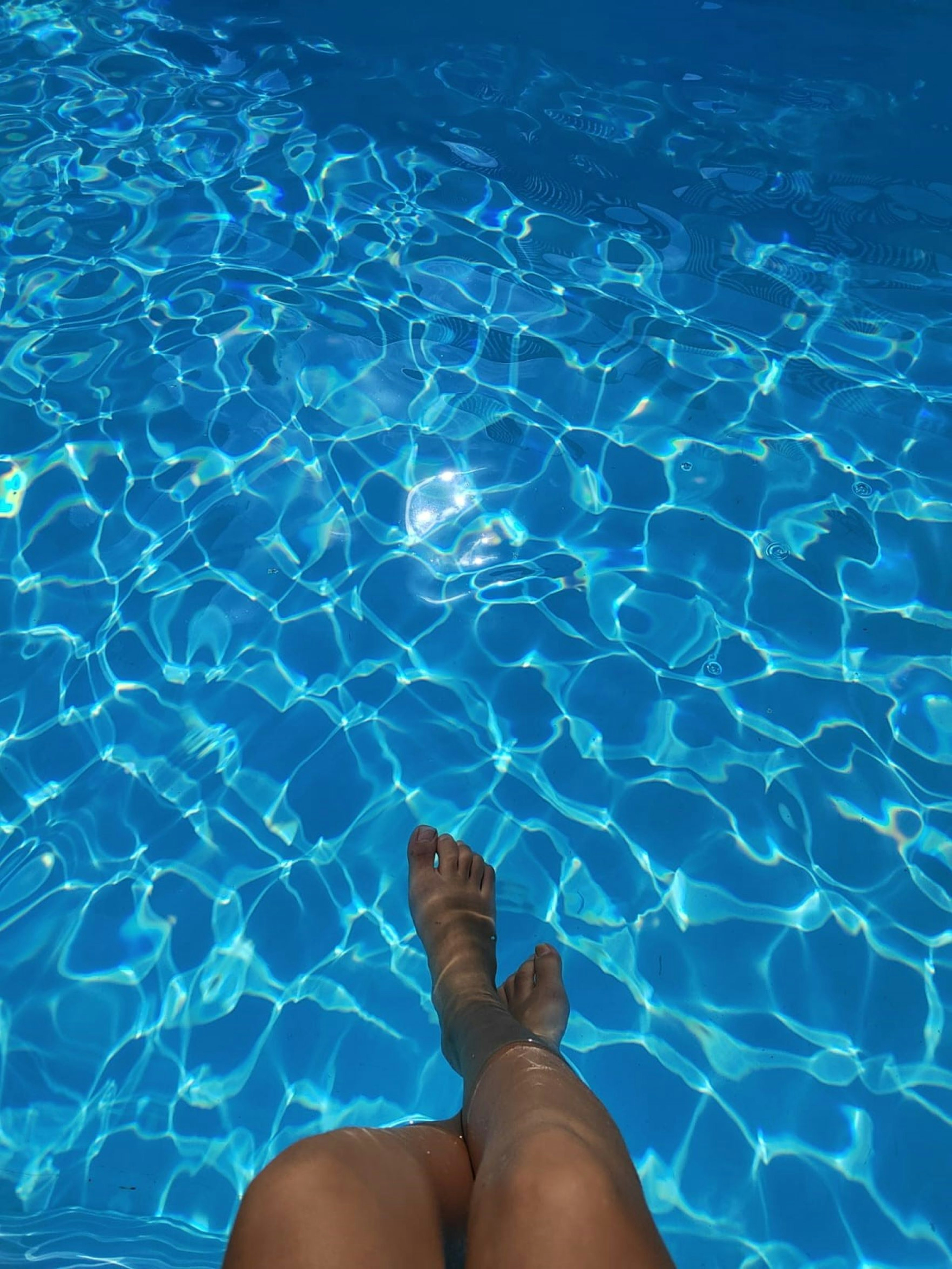 Piedi immersi in acqua blu scintillante della piscina