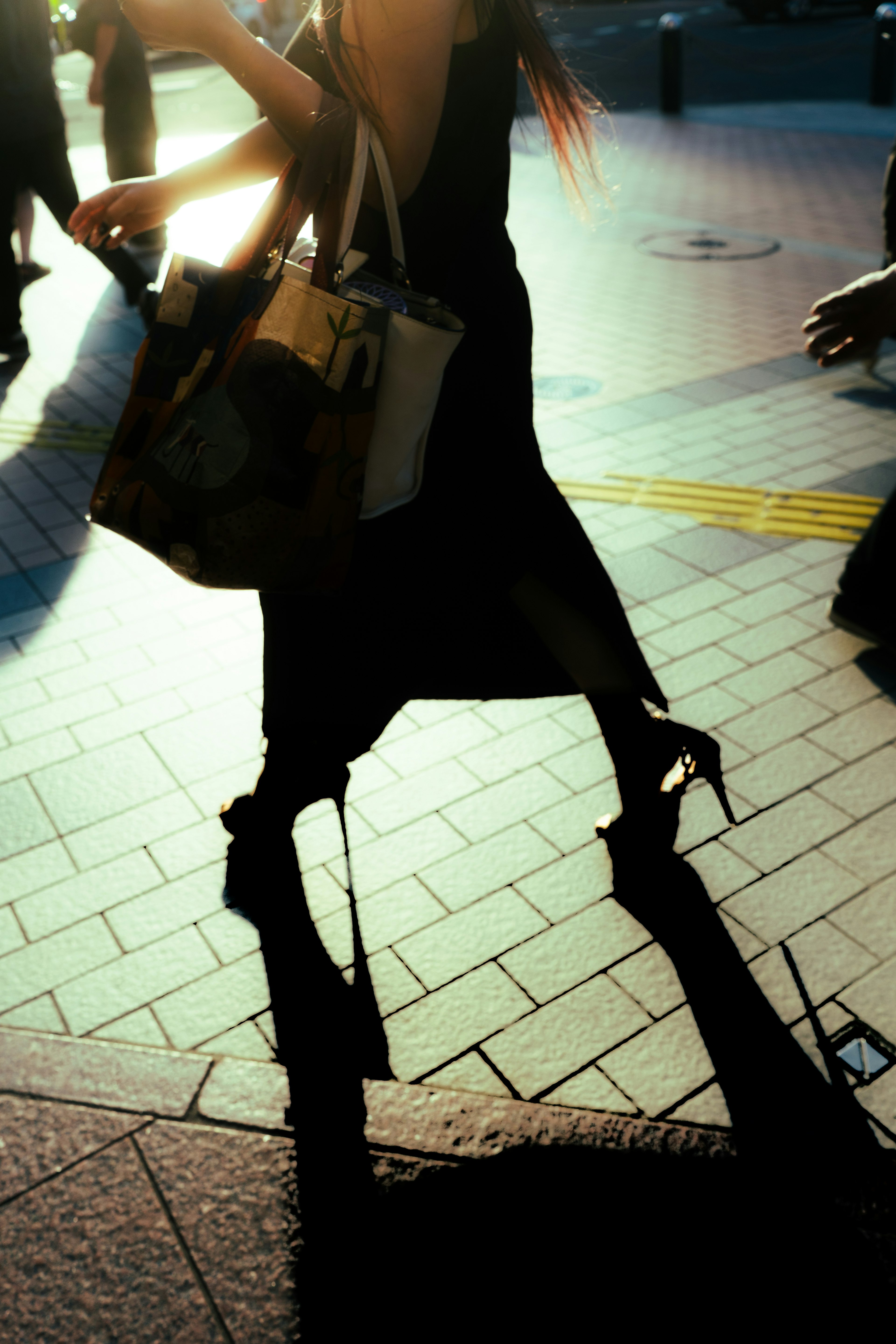 Une femme en robe noire marche en talons hauts projetant une ombre sur la rue