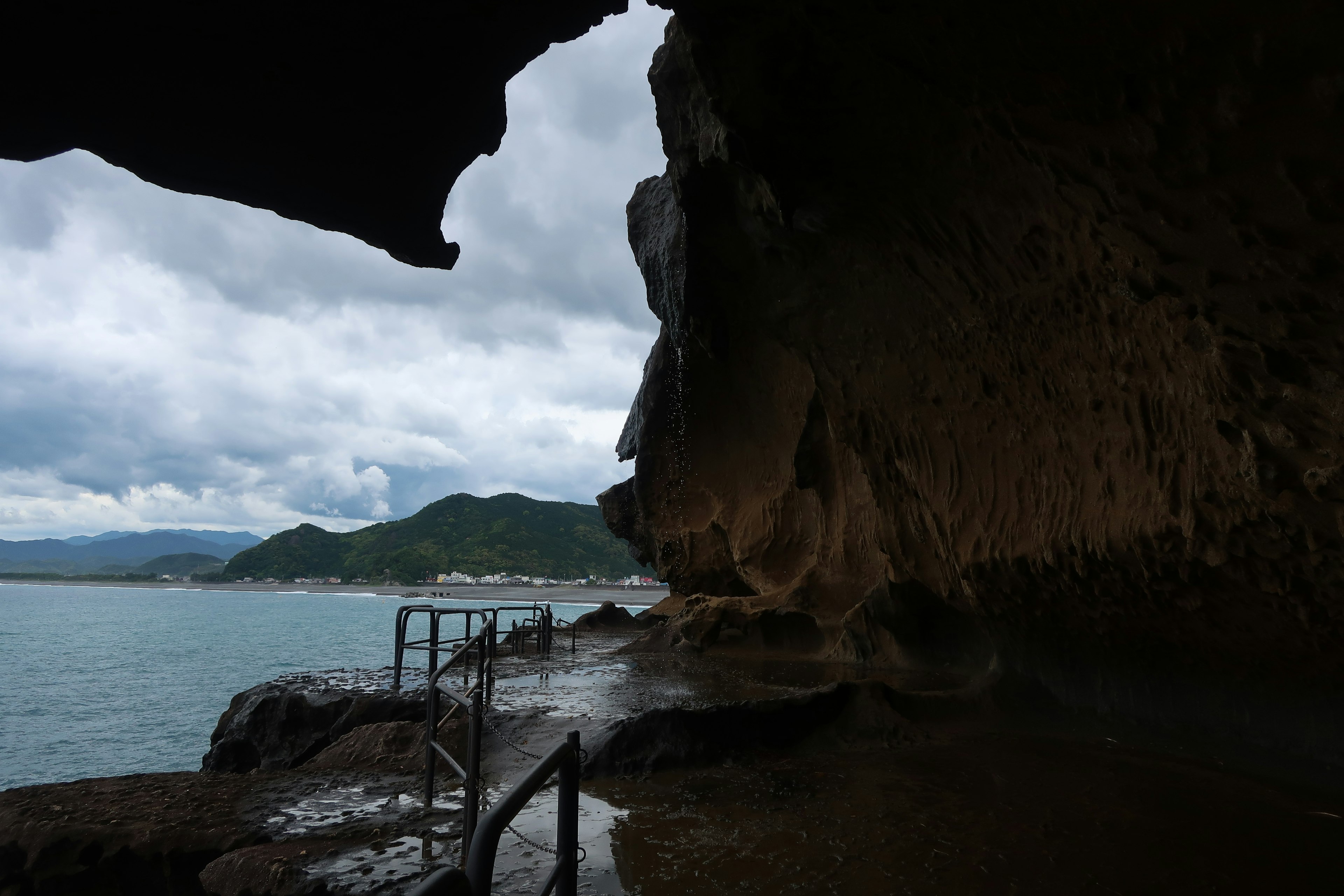 Vista dall'interno di una grotta marina con cielo nuvoloso e costa lontana con barche