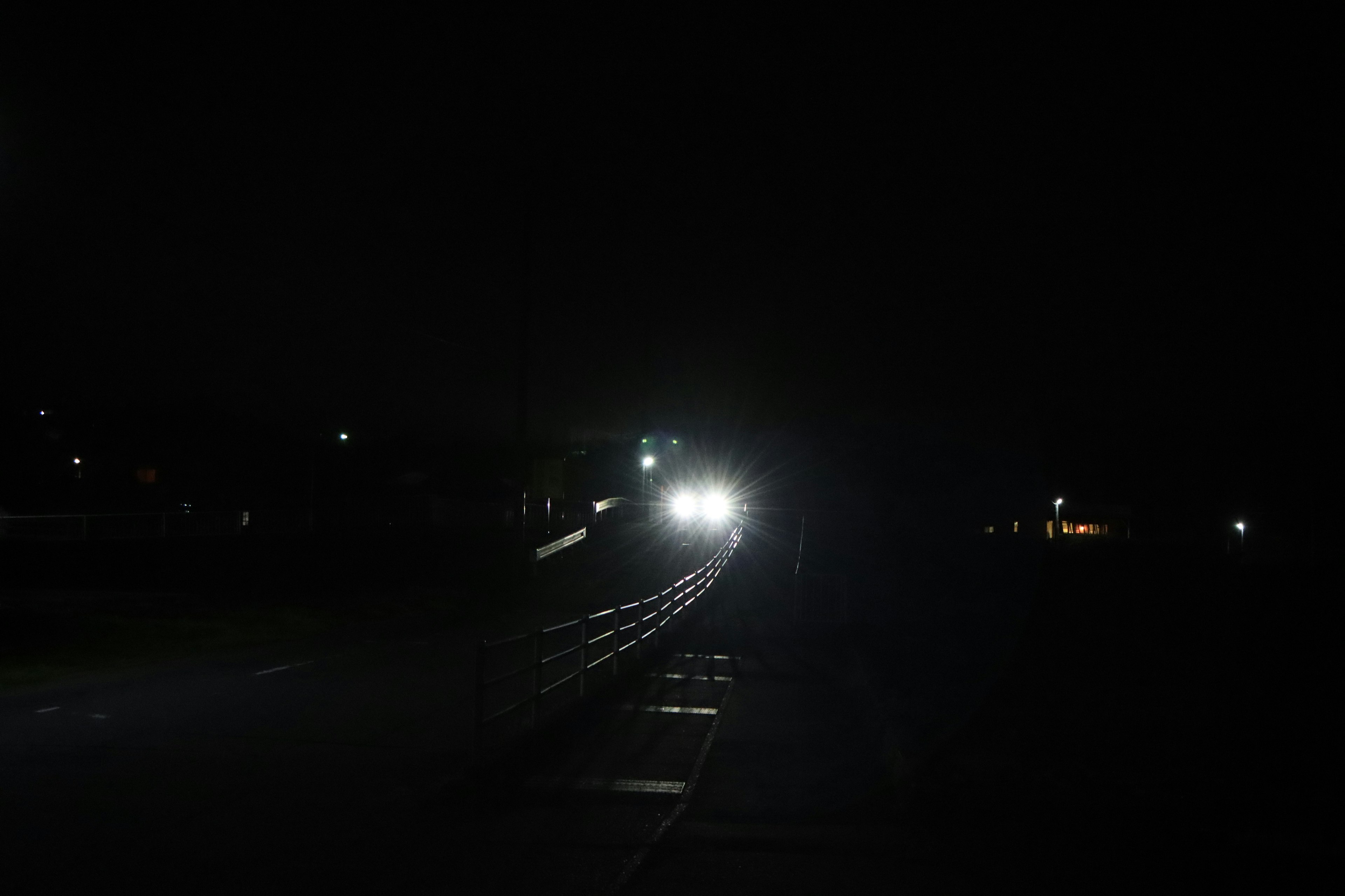 Car headlights shining in a dark night with a road