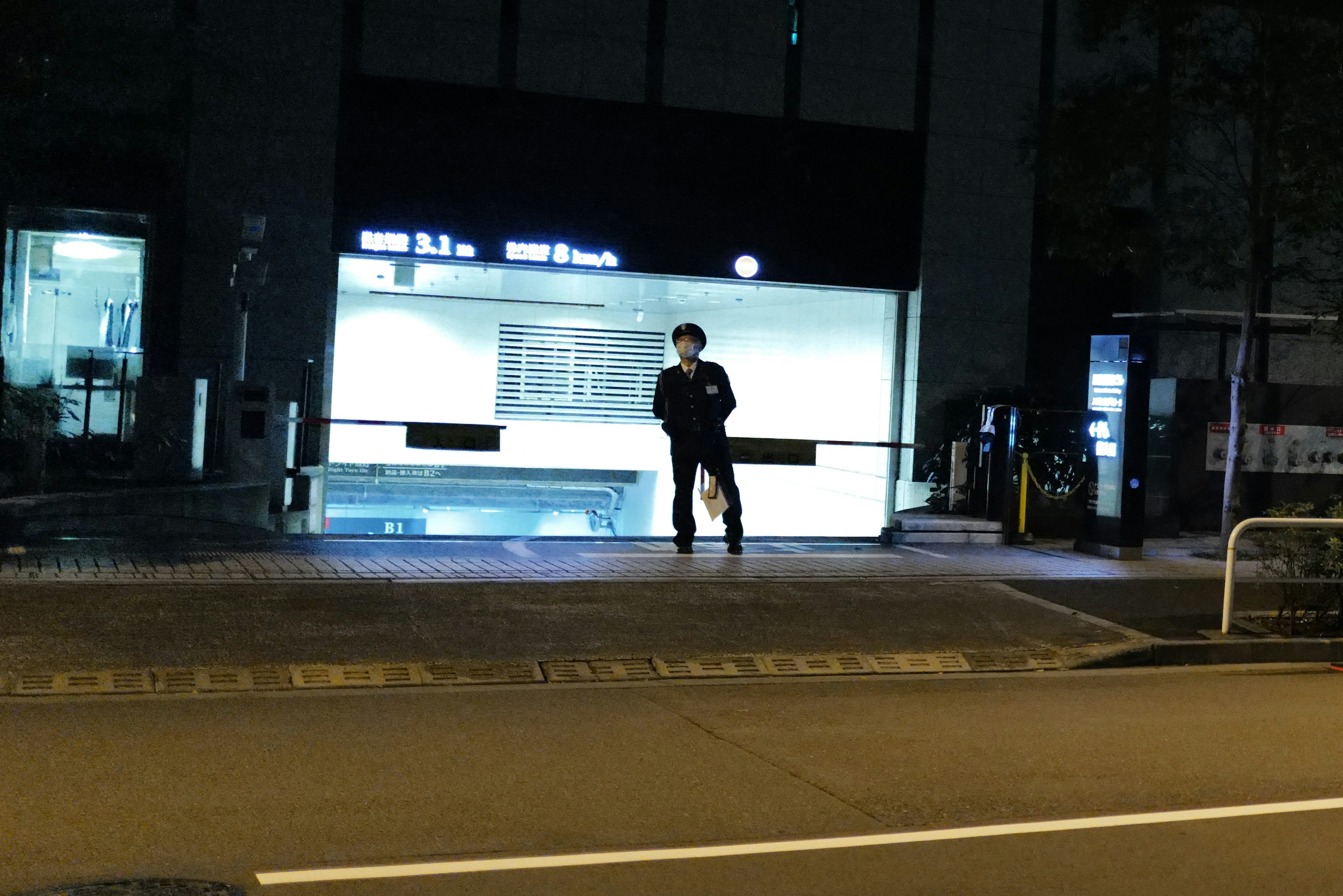 夜の駅の前に立つ人物と明るい掲示板