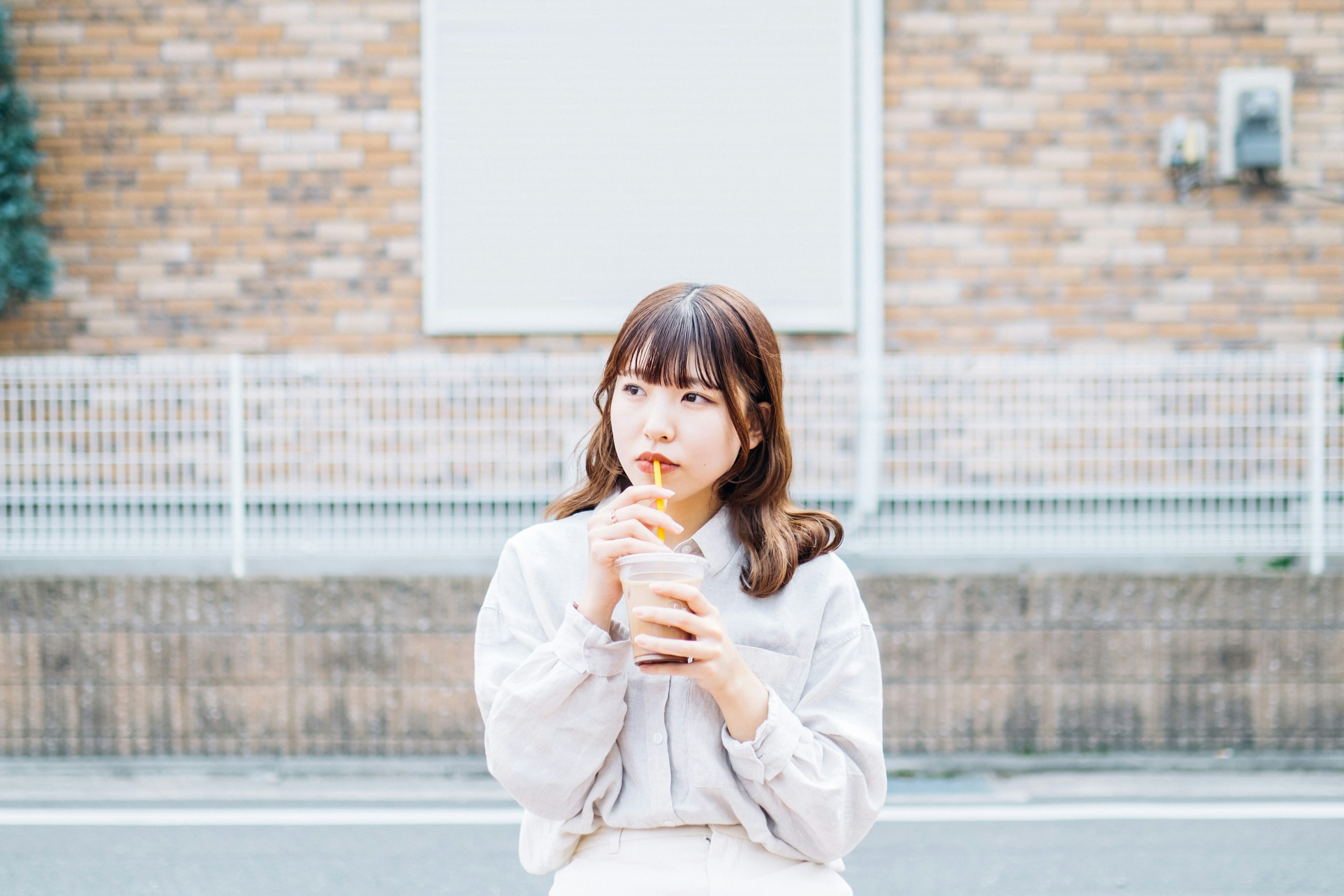 A woman holding a drink while contemplating against a brick wall background