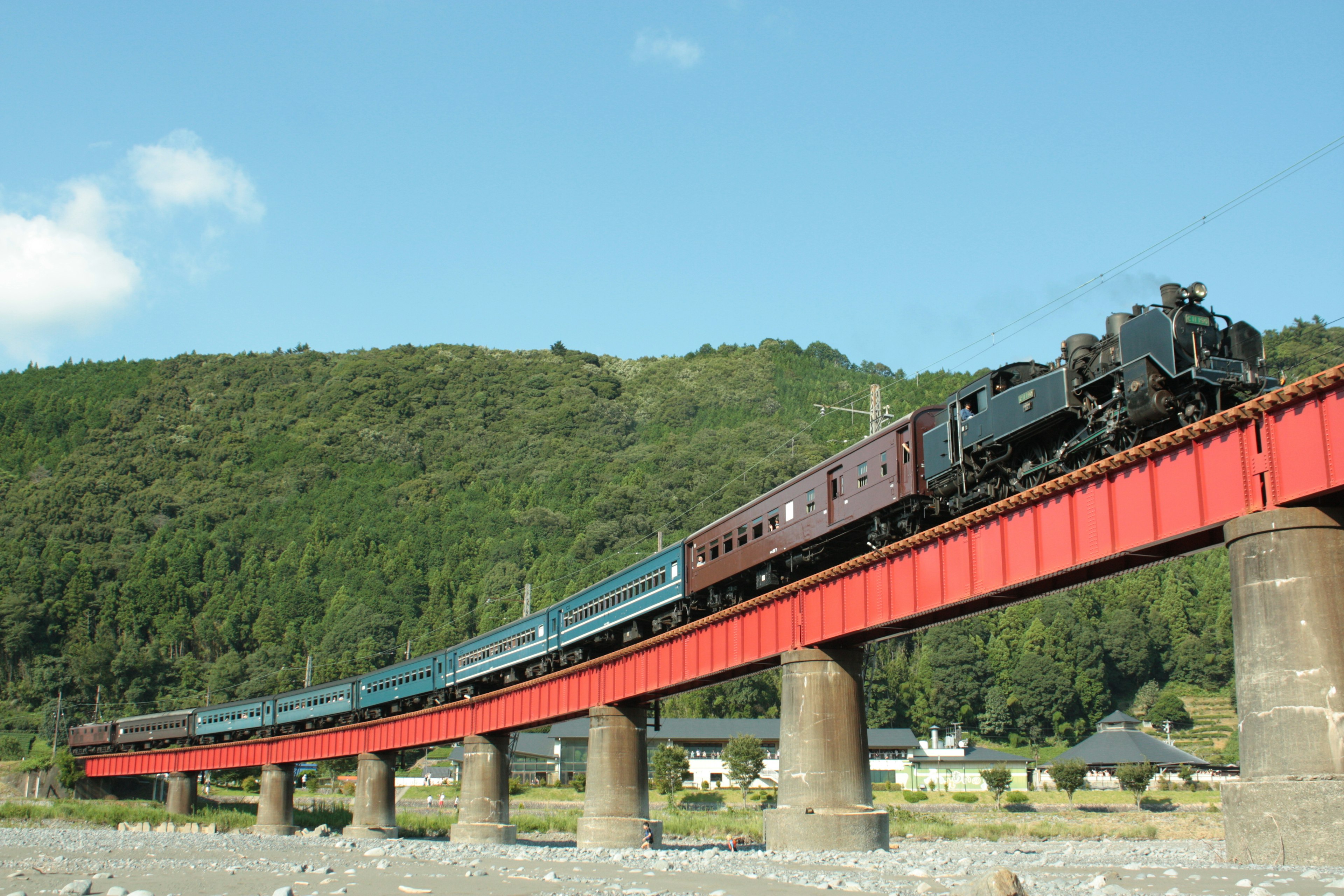 Steam locomotive crossing a red bridge with passenger cars