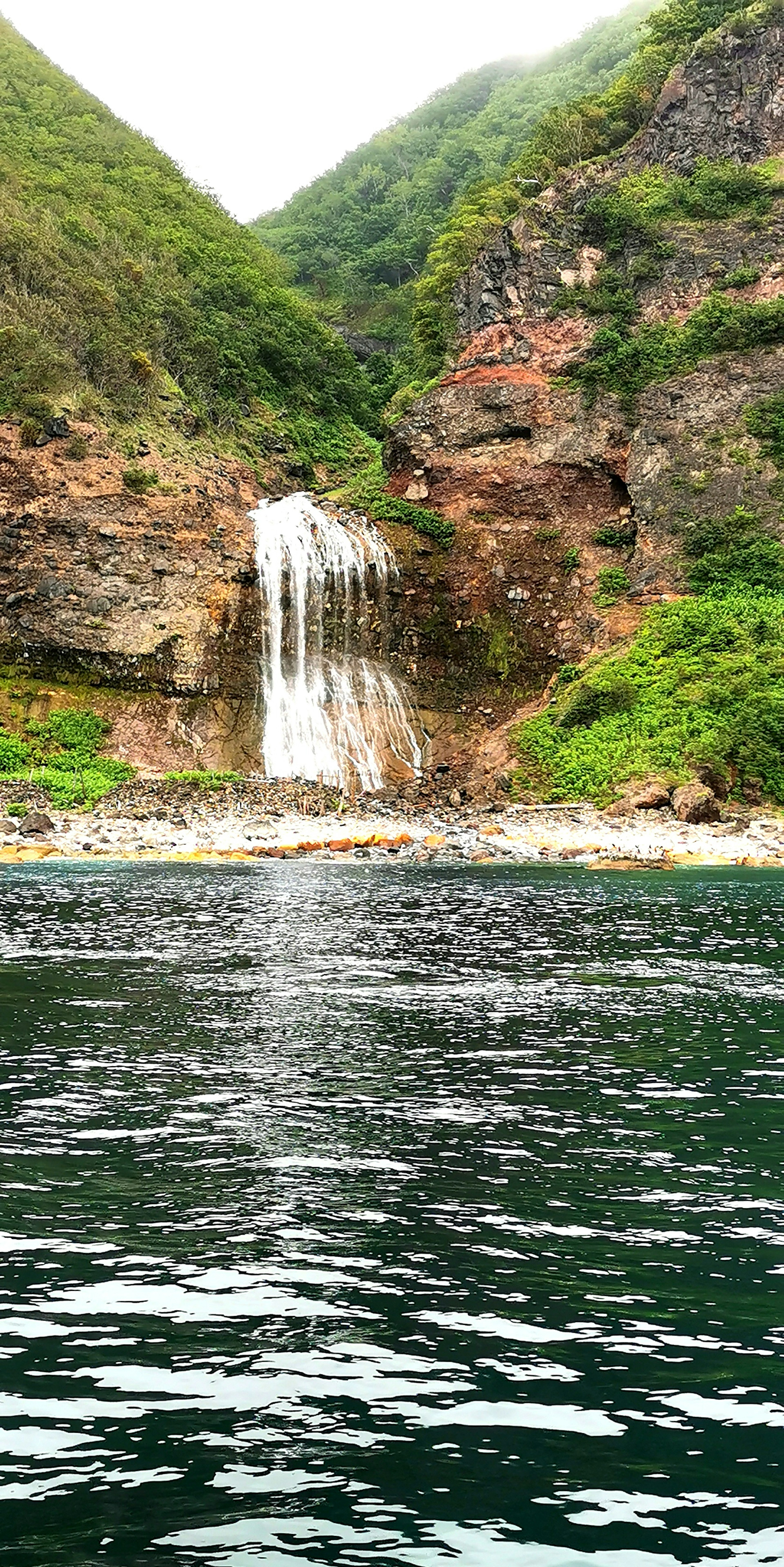 Vue panoramique d'une cascade entre des collines verdoyantes et un lac tranquille