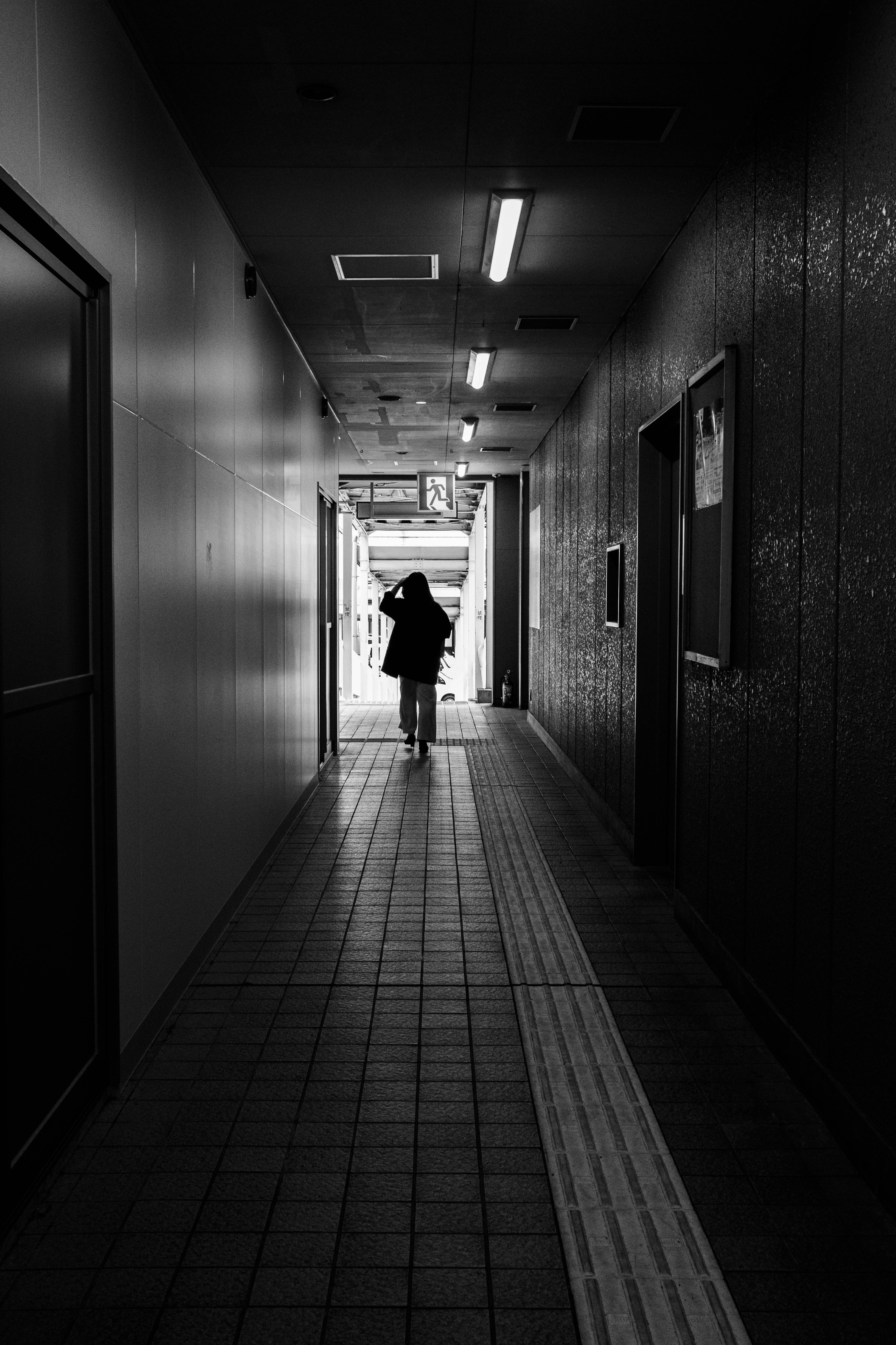 Silhouette of a person walking in a dark hallway with a bright exit