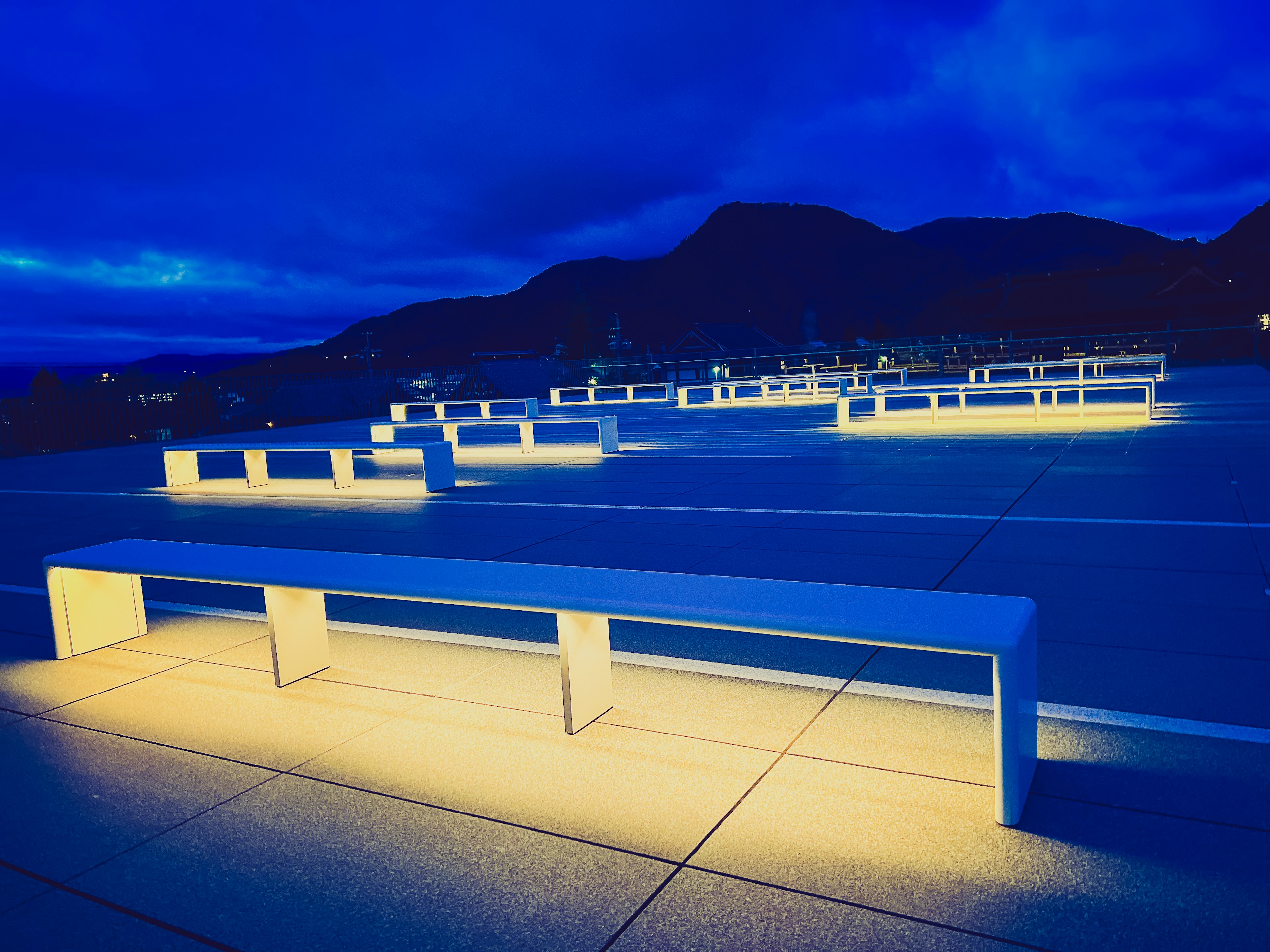 Panchine bianche illuminate sotto un cielo notturno blu con silhouette di montagne