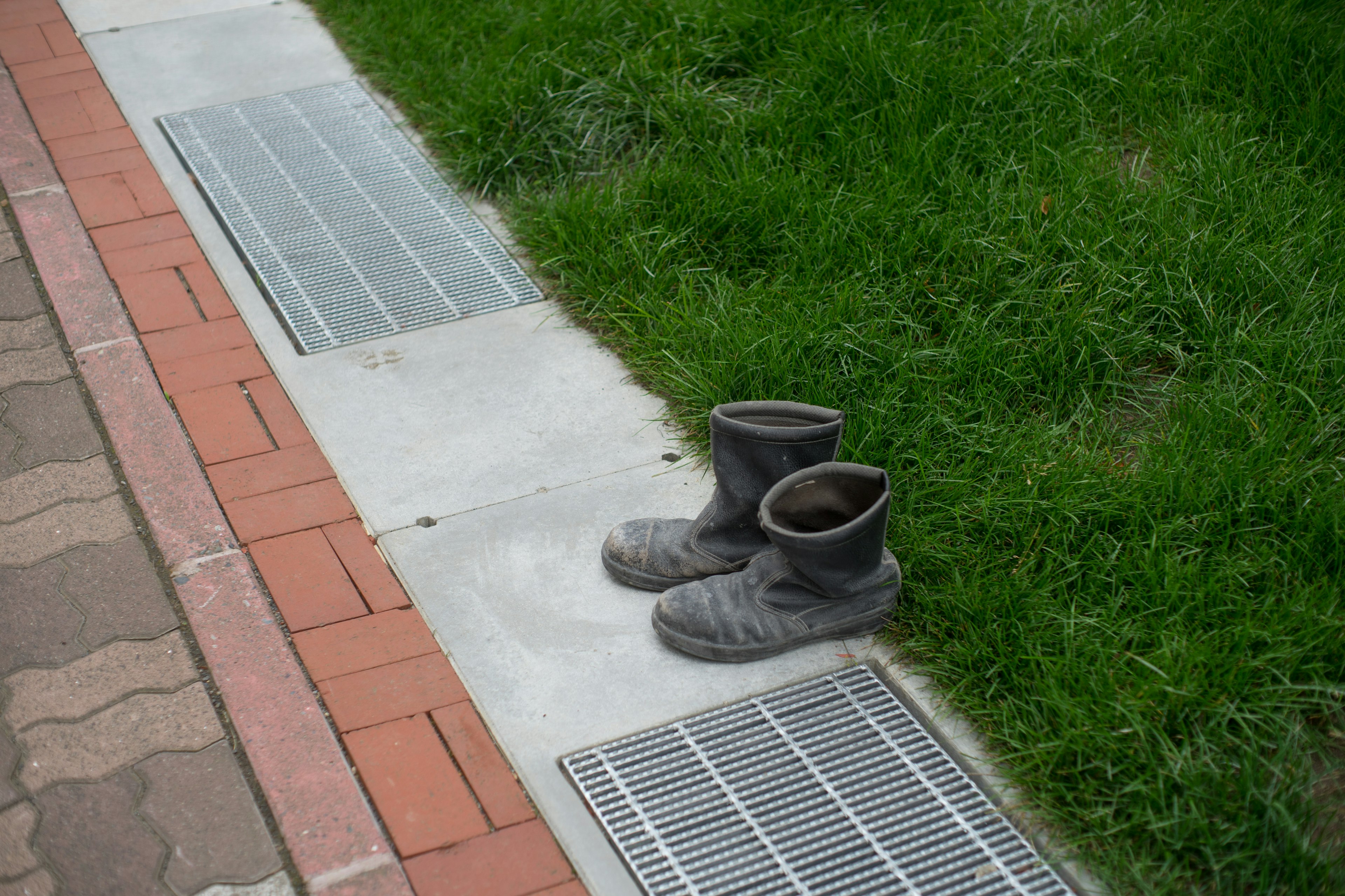 Dirty boots placed on grass next to a paved pathway