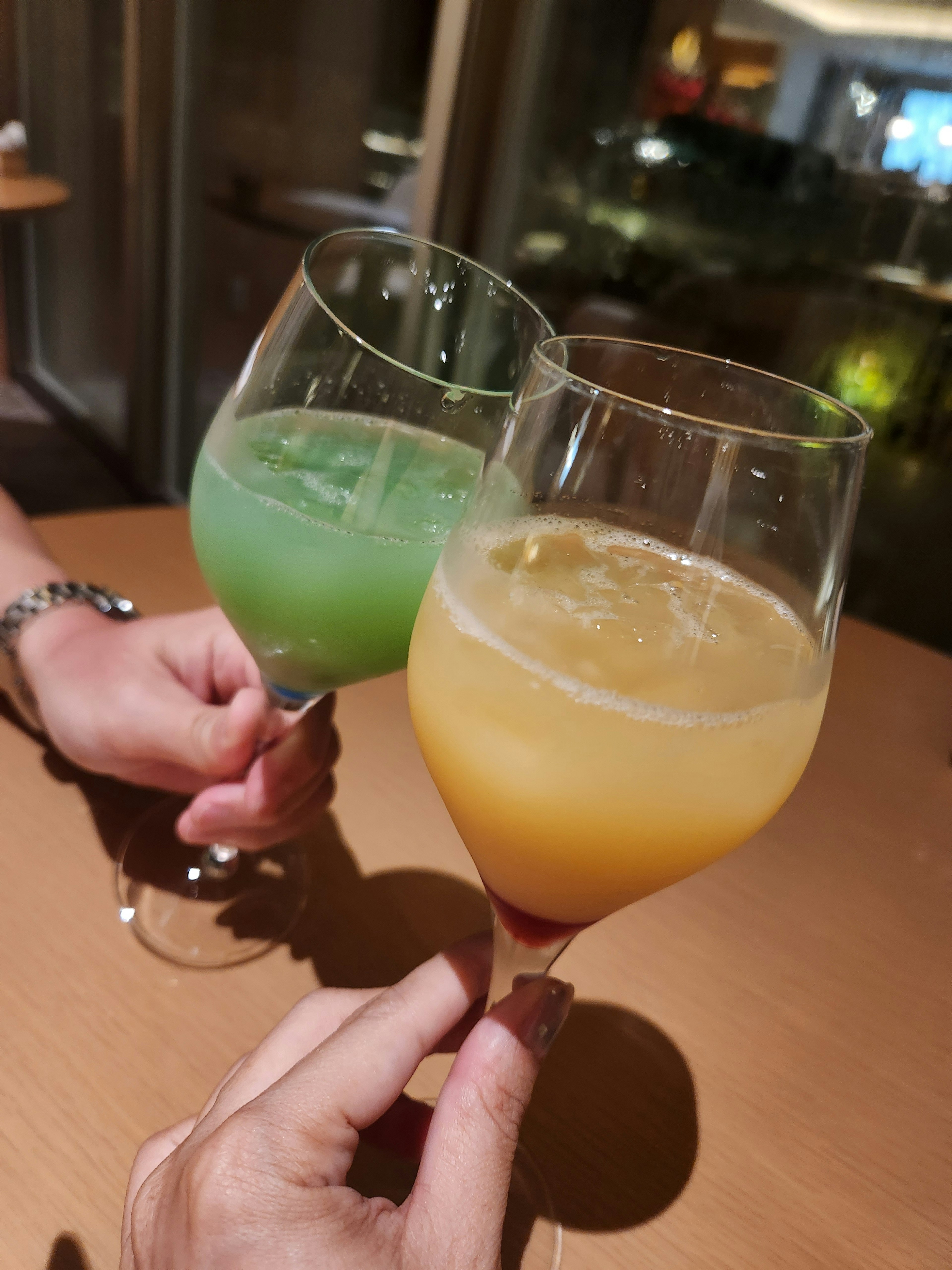 Hands holding glasses of green and orange cocktails