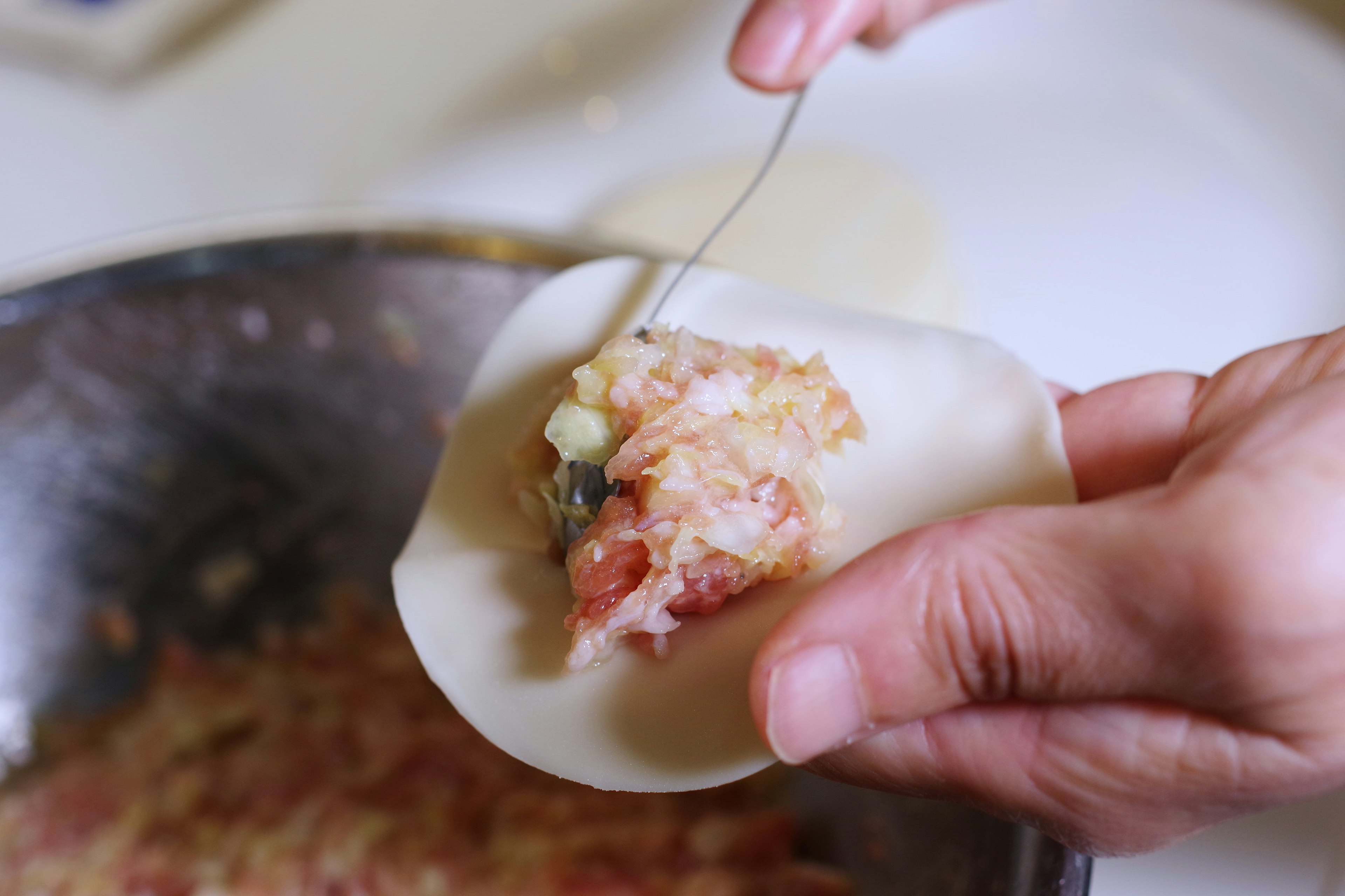 A hand placing filling onto a dumpling wrapper