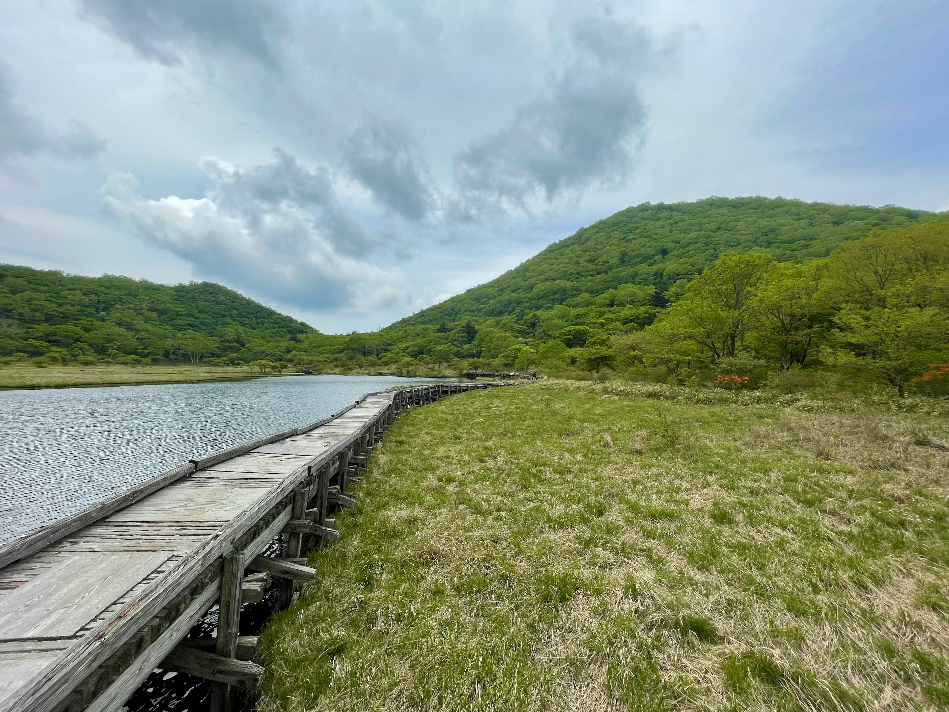 绿色山丘和宁静水面的风景，湖边有一条木栈道