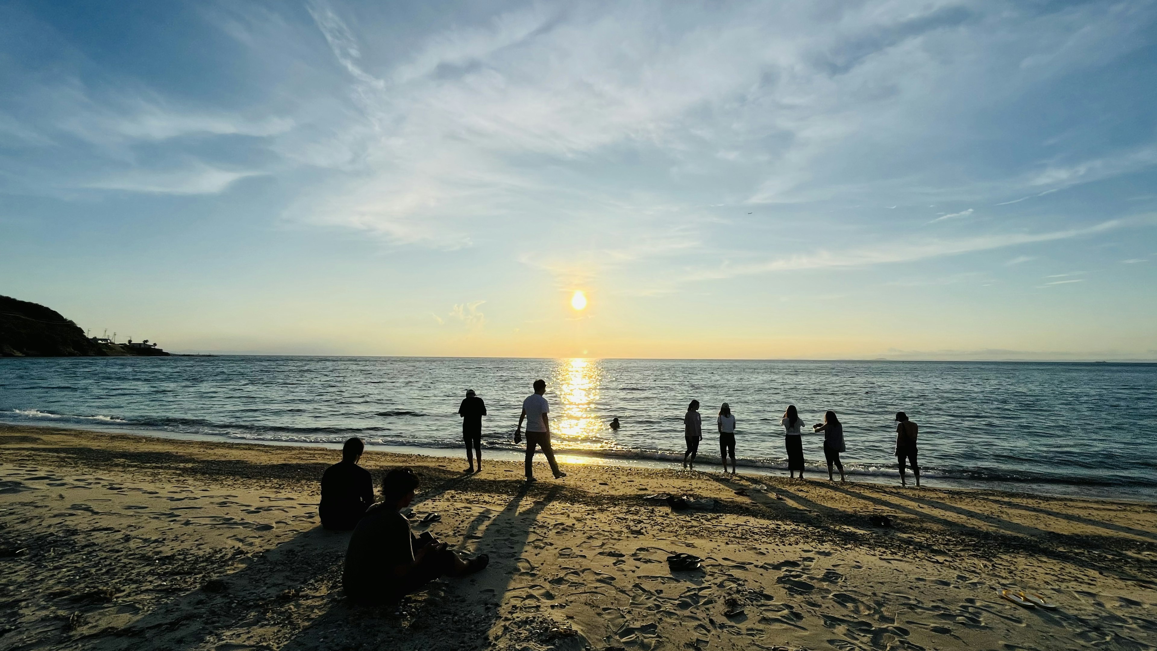 夕日を背景に海辺で立つ人々のシルエット