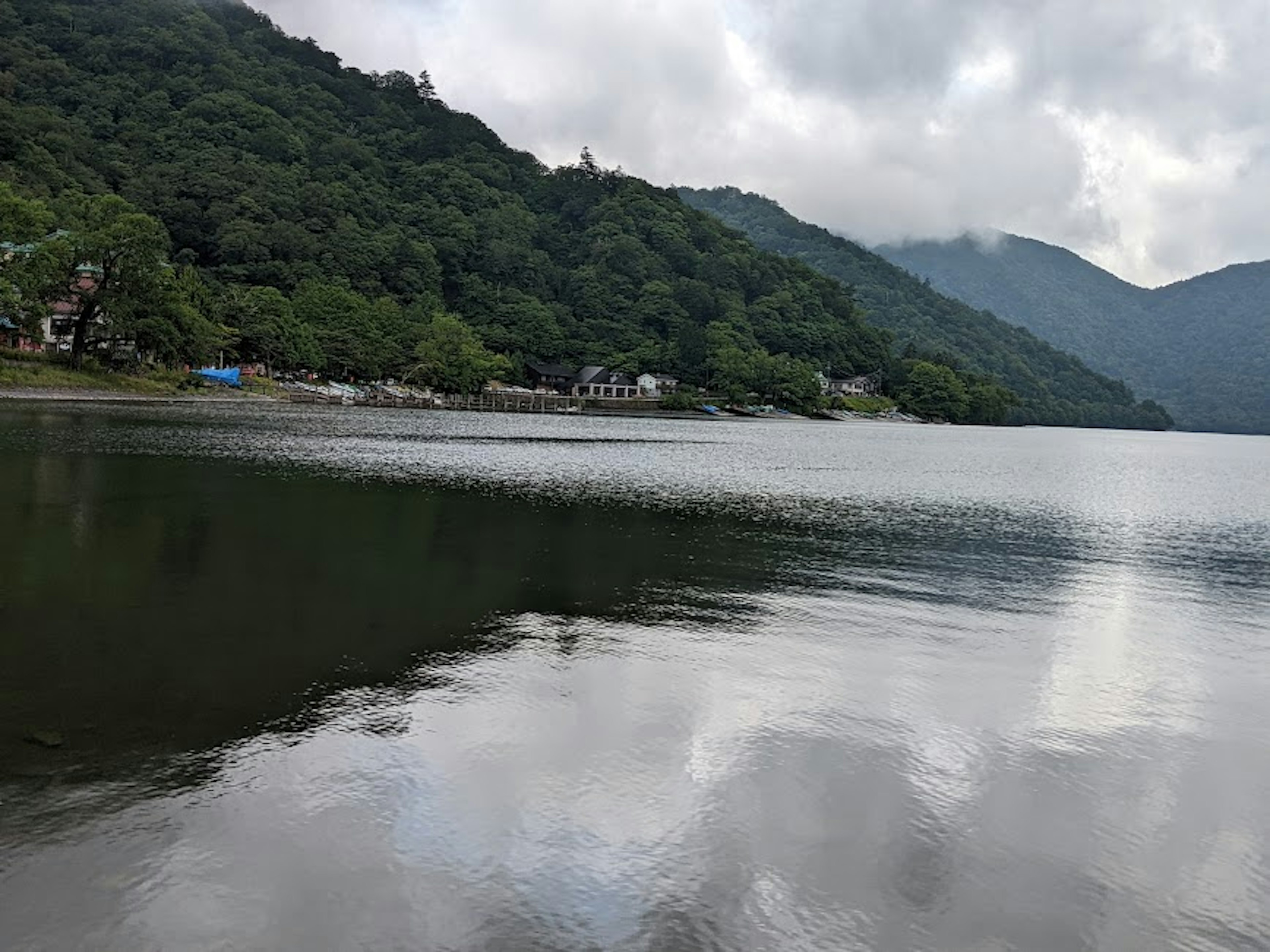 Danau tenang yang memantulkan gunung hijau di bawah langit mendung