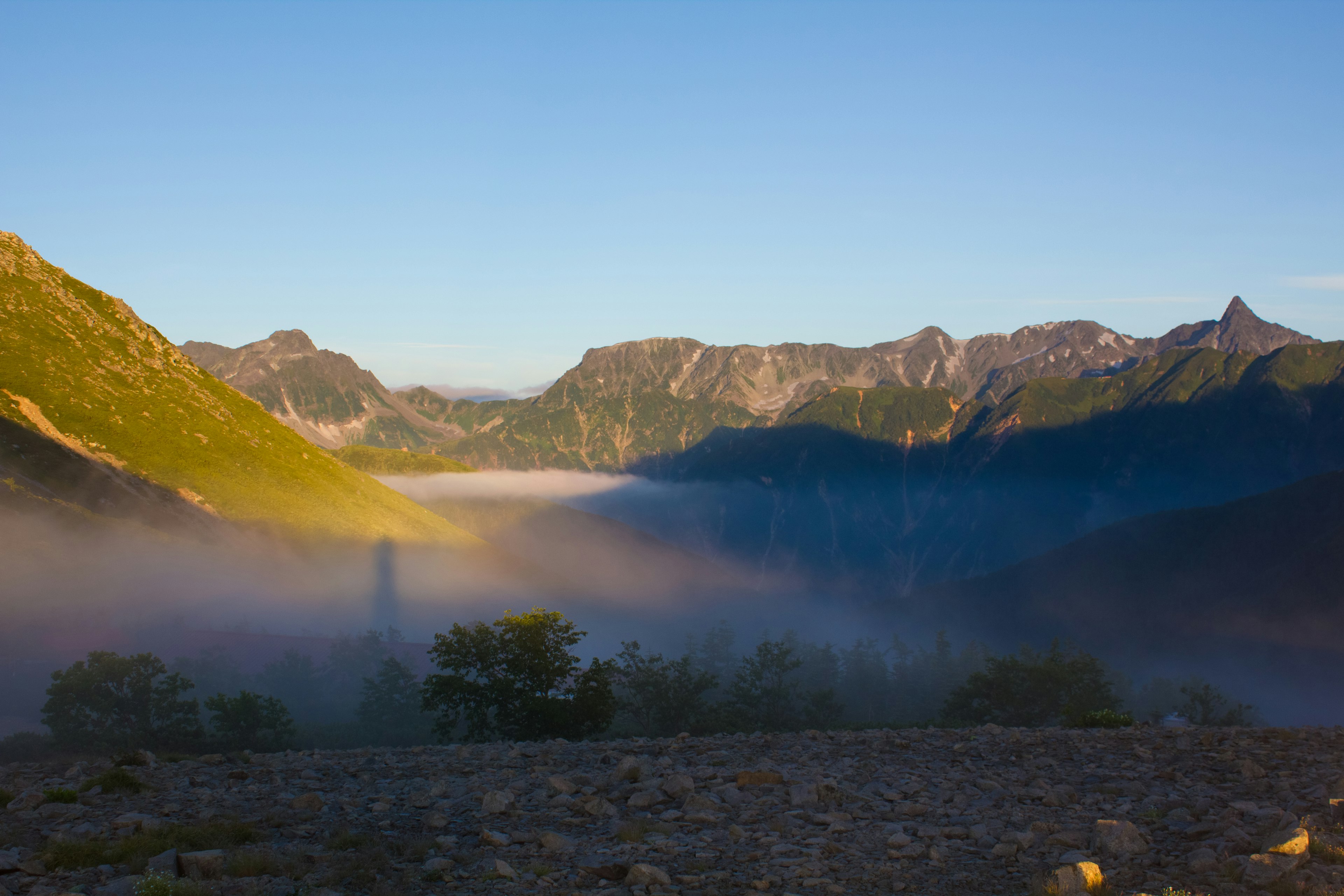 Paisaje montañoso envuelto en niebla con un cielo azul claro