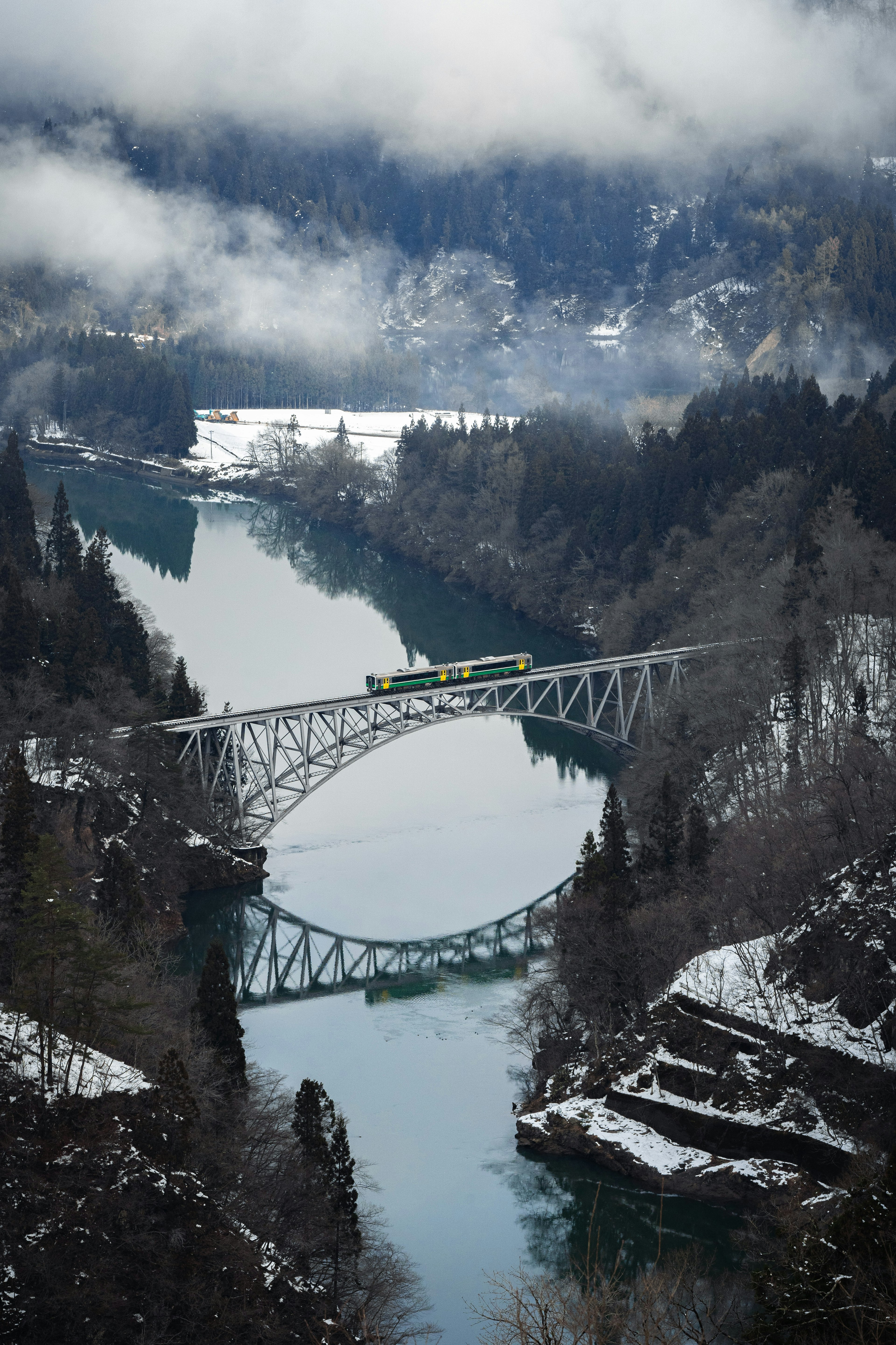 Una vista panoramica di un ponte su un fiume circondato da montagne innevate e nebbia