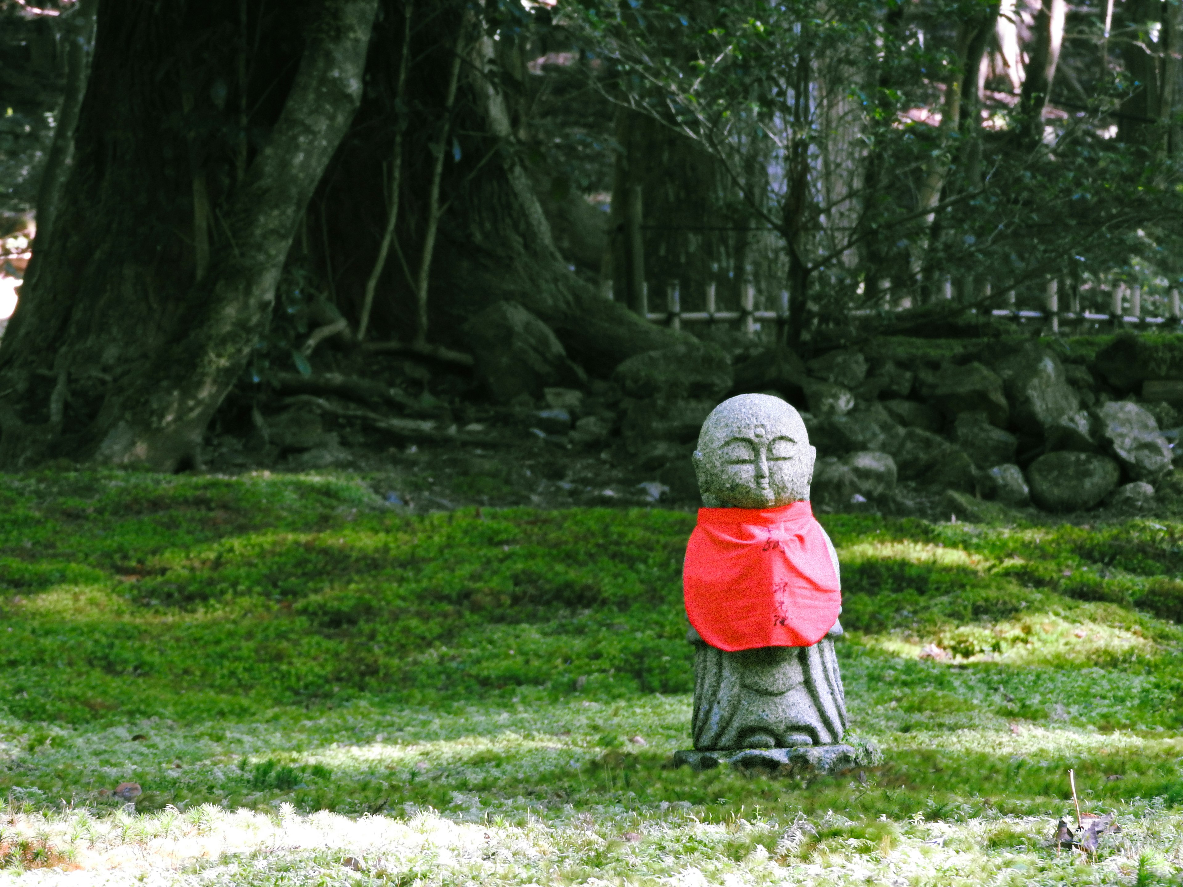 Steinstatue mit rotem Umhang, die im grünen Gras steht