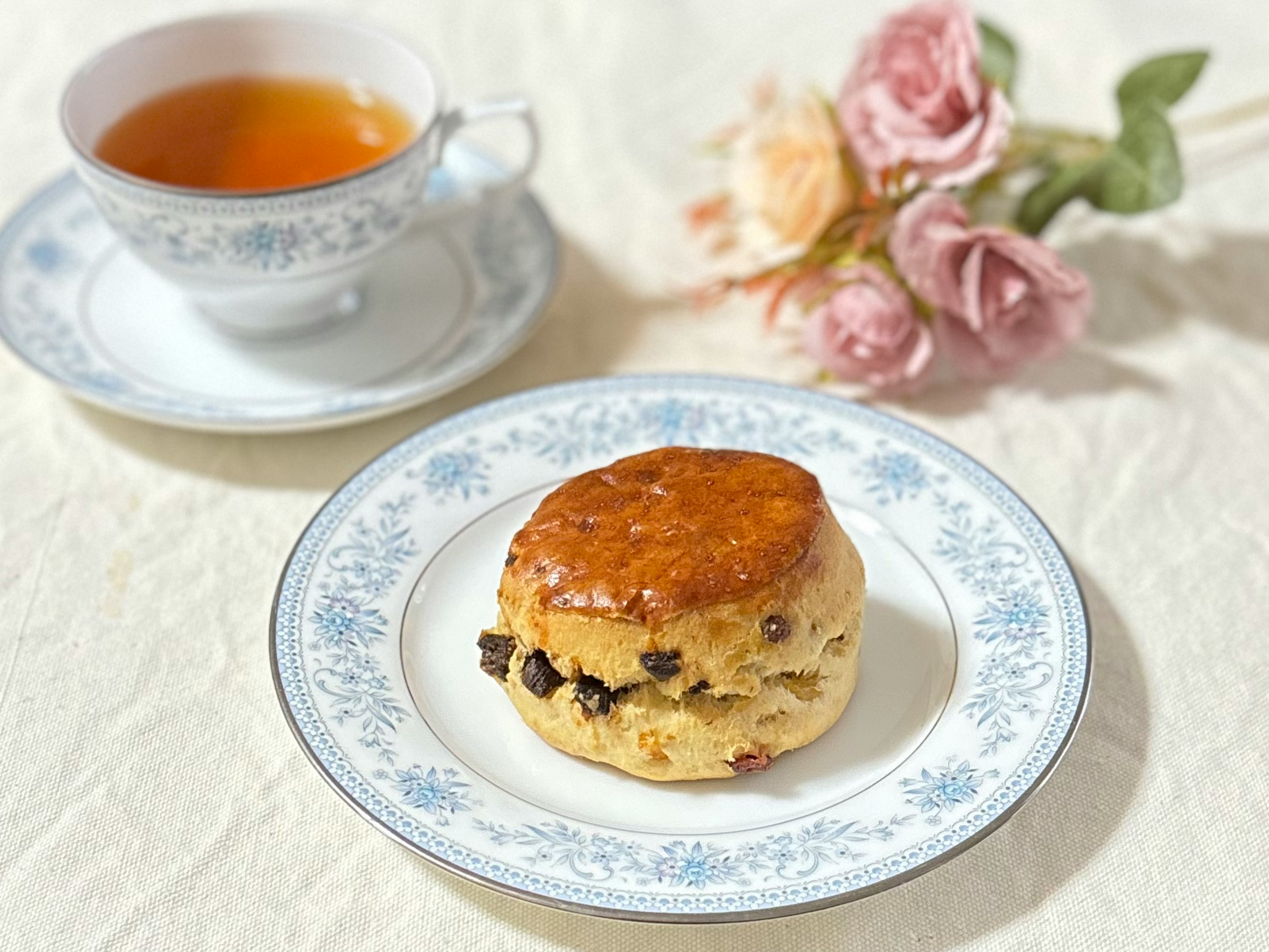 Piring dengan scone dan secangkir teh di atas meja yang didekorasi dengan bunga