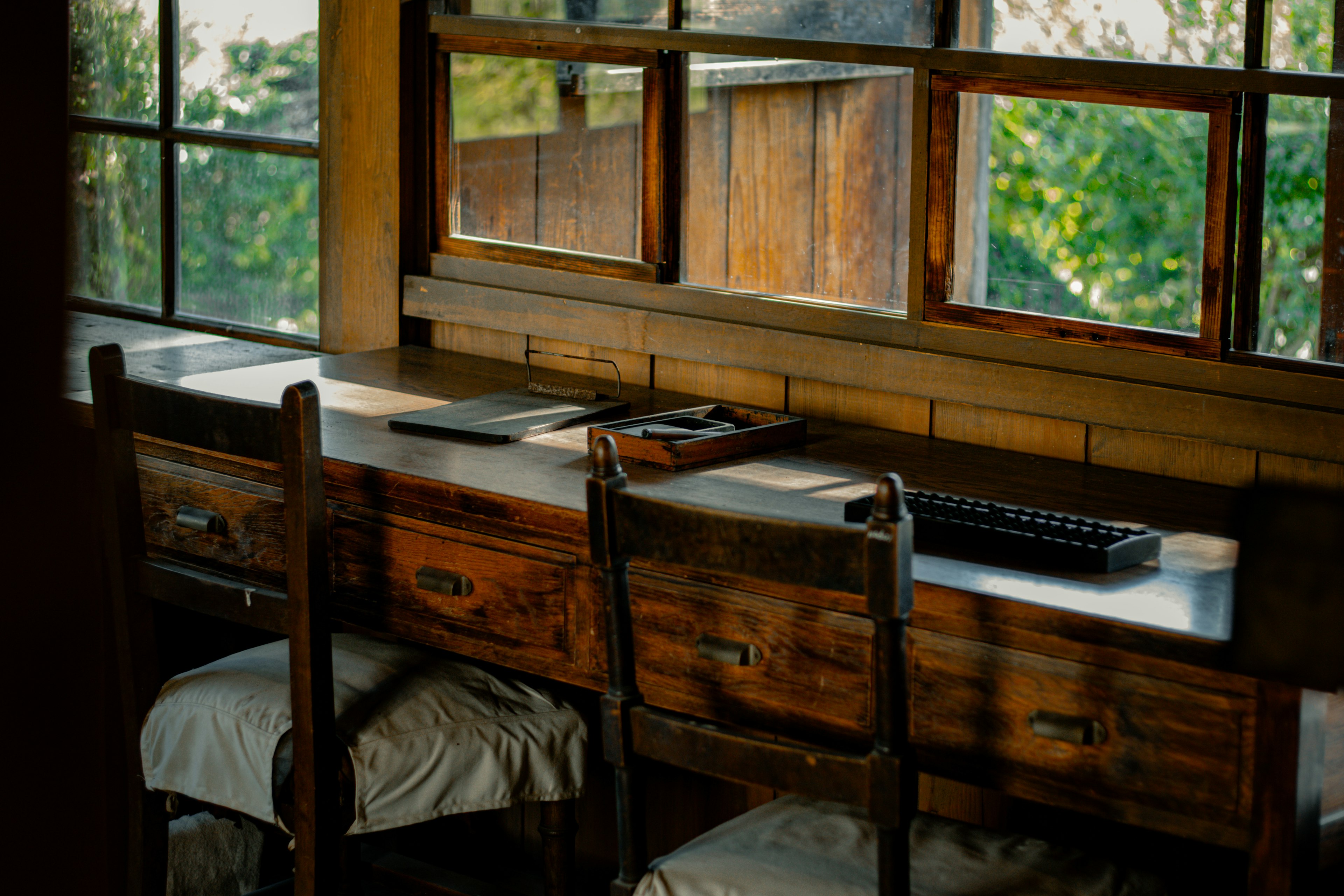 Espacio de trabajo tranquilo con escritorio y sillas de madera vista verde a través de las ventanas